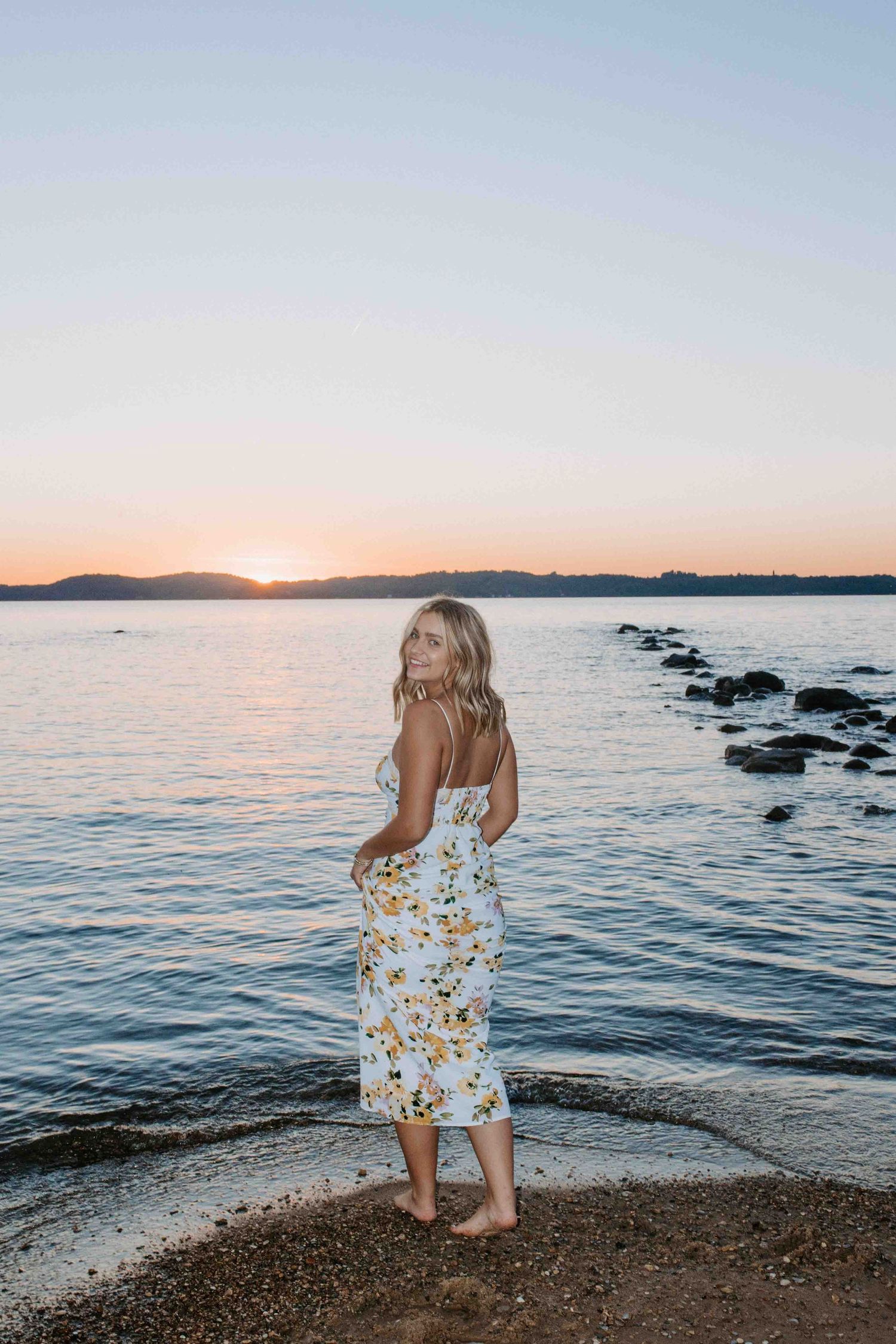 A person in a floral dress stands at the beach during golden hour sunset.