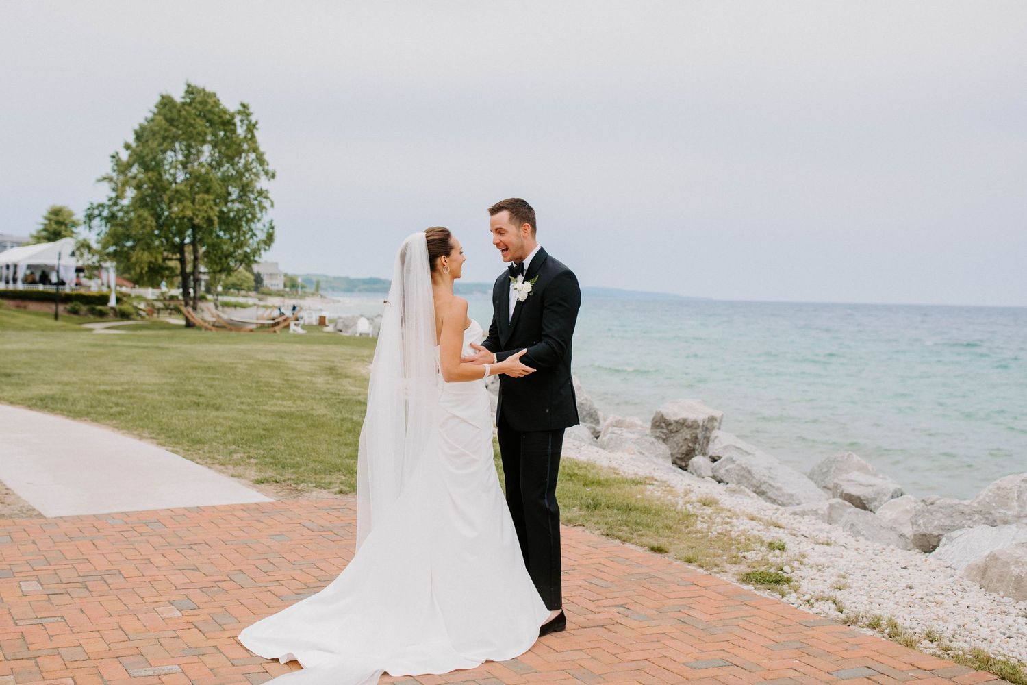 Couple in wedding attire poses against scenic coastal backdrop.