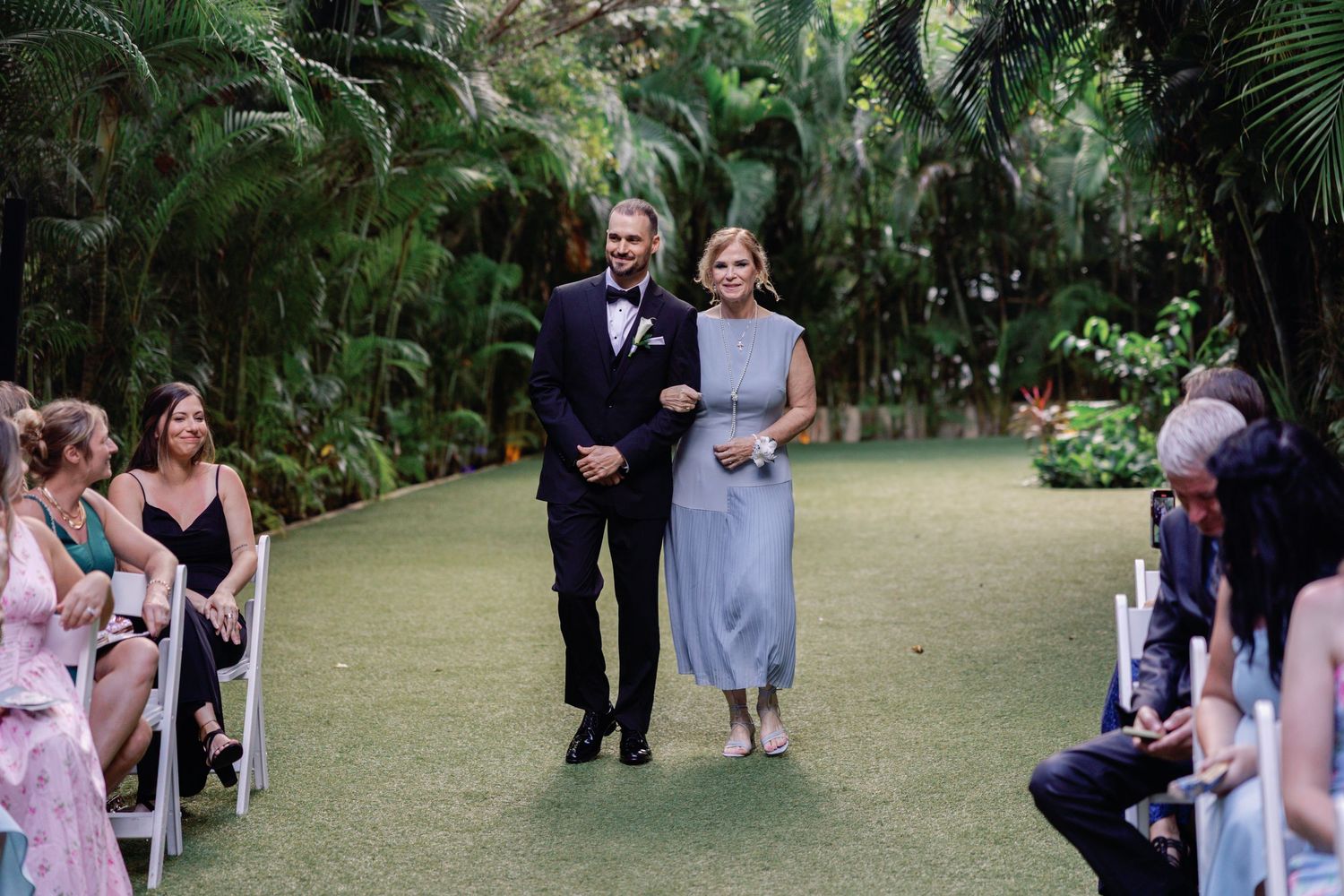 Wedding guests gather on lush green lawn during outdoor ceremony.