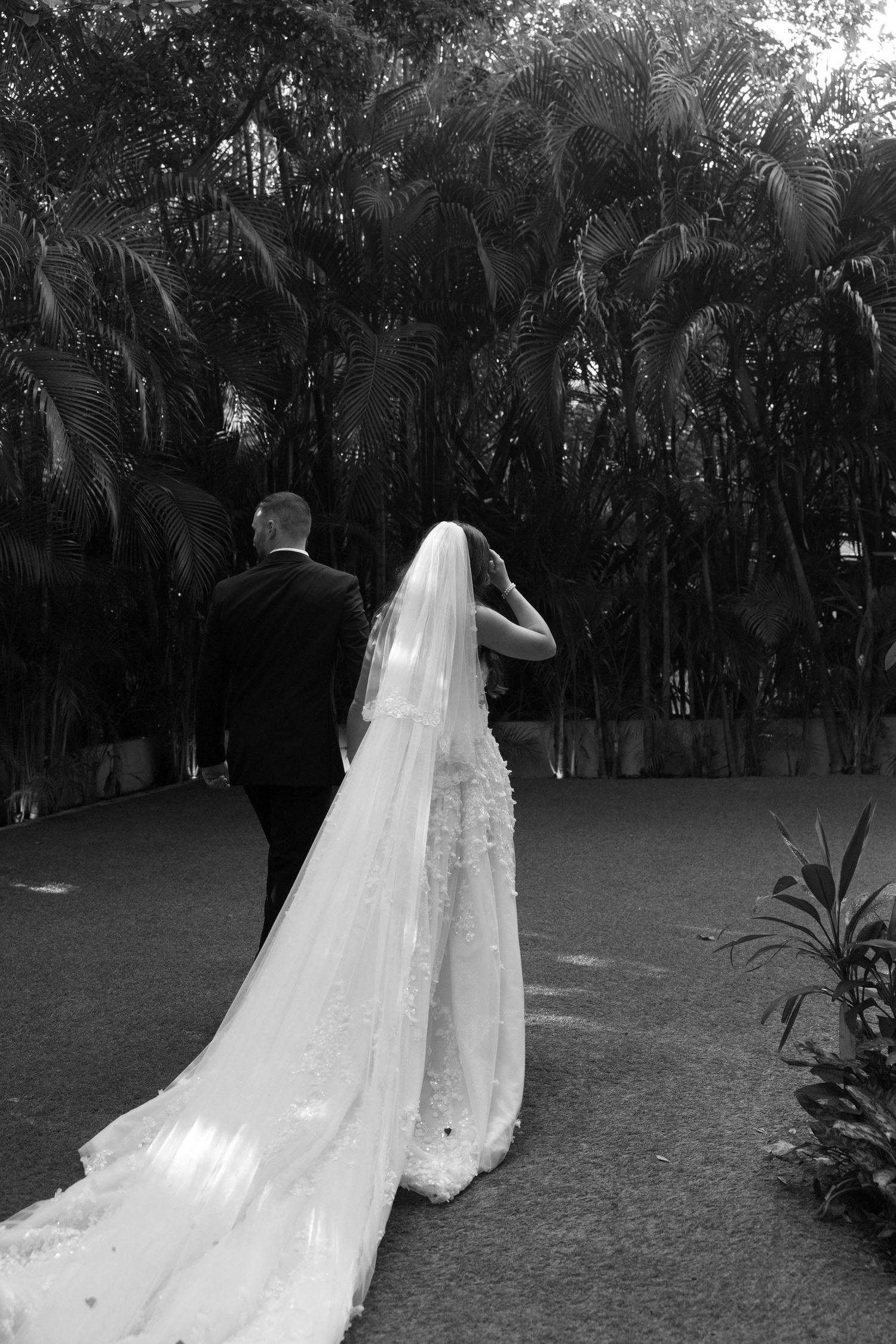 Wedding dress with flowing veil photographed in a lush garden setting.