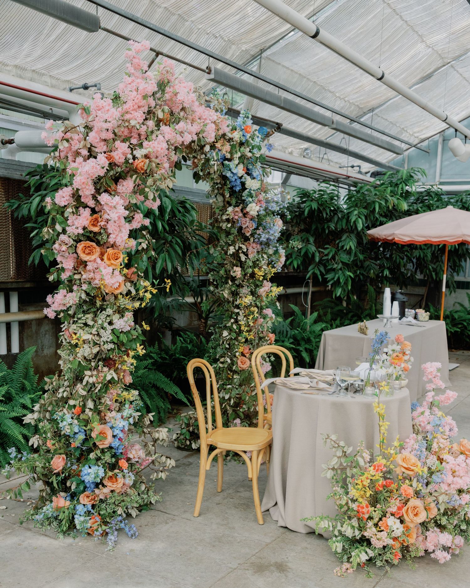 Reception setup with pastel floral arrangements and wooden chairs under clear tent.