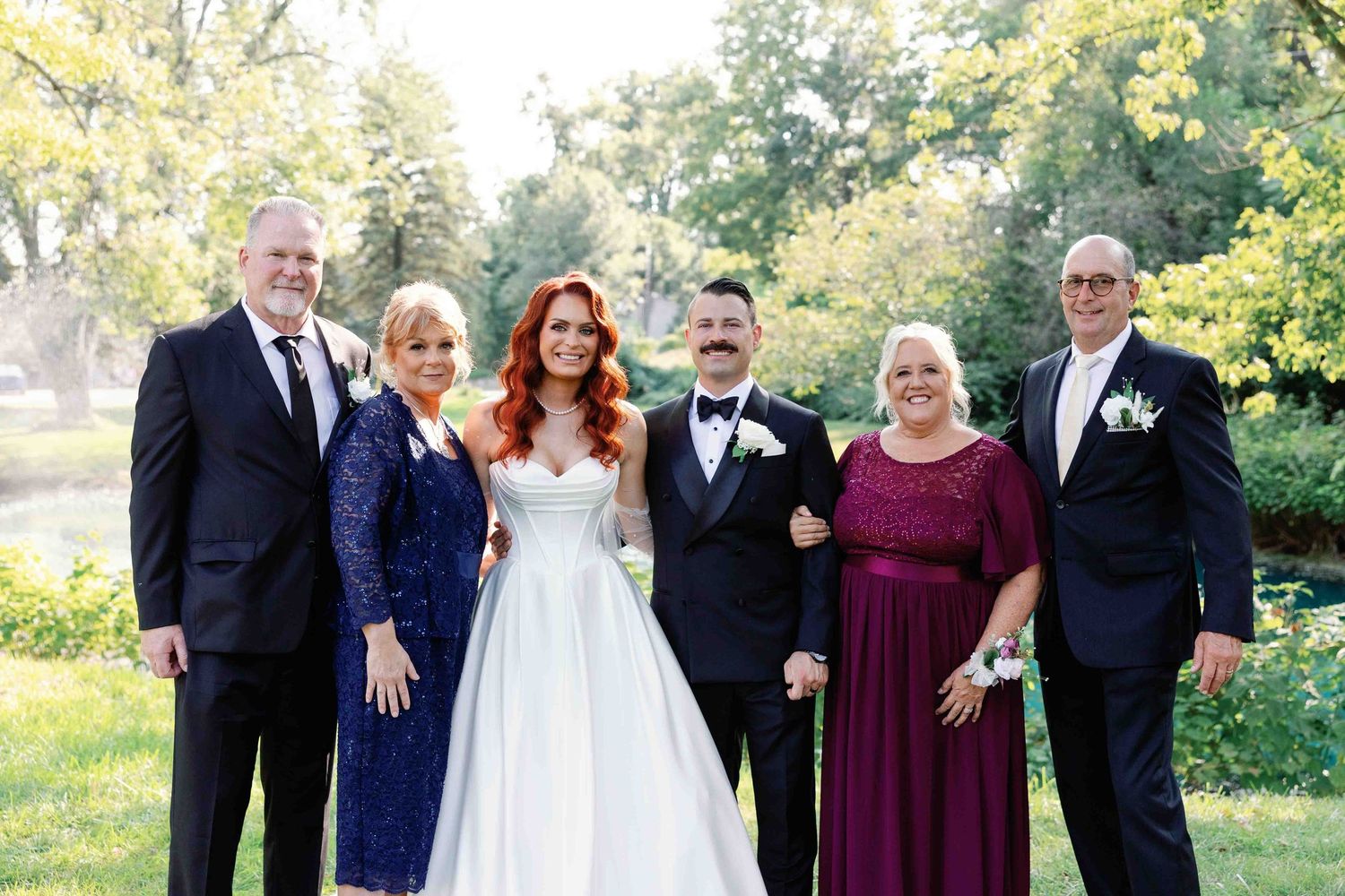 A formal wedding party poses together outdoors in elegant attire.
