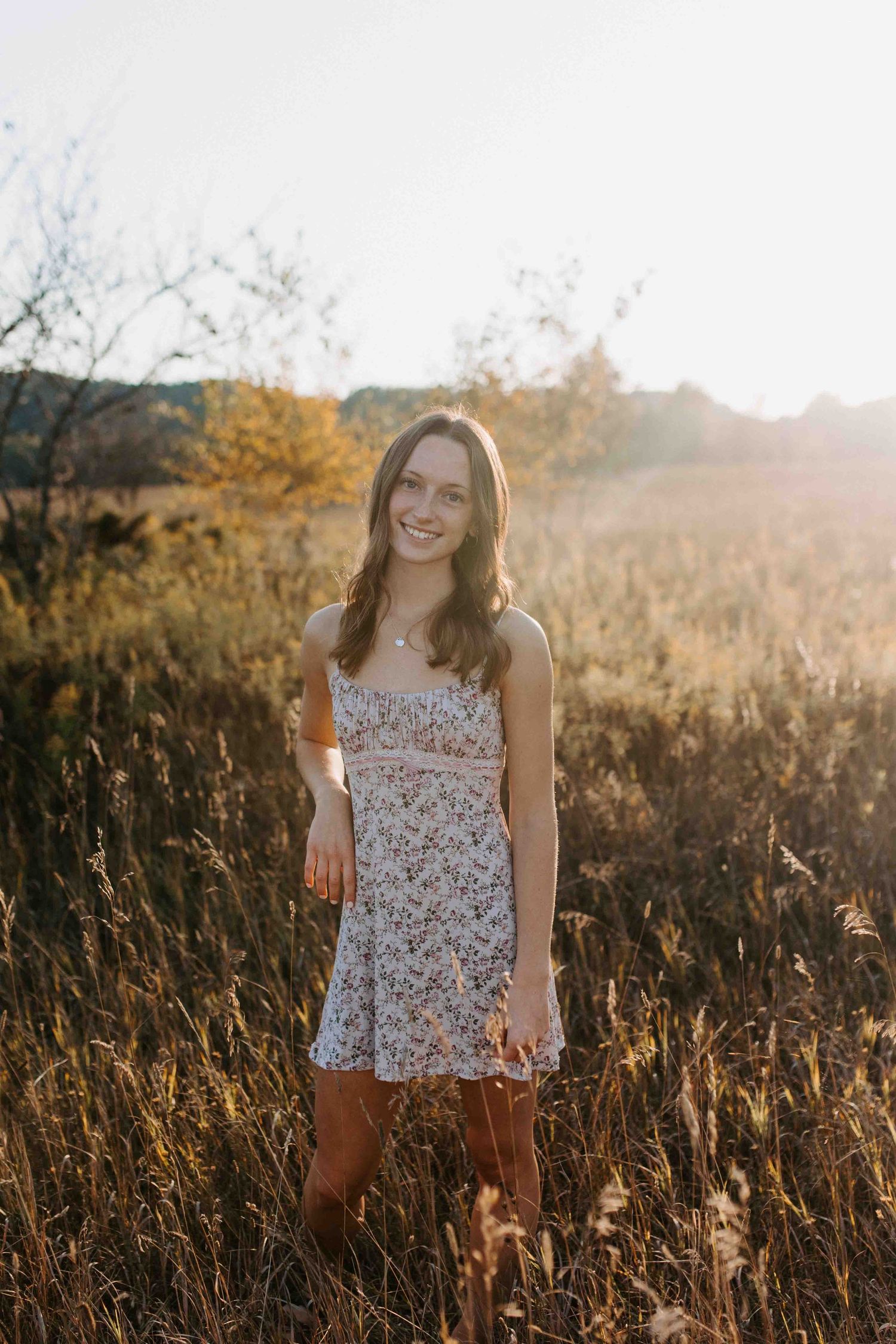 Sunset field portrait with golden light streaming through tall grass and a floral summer outfit.
