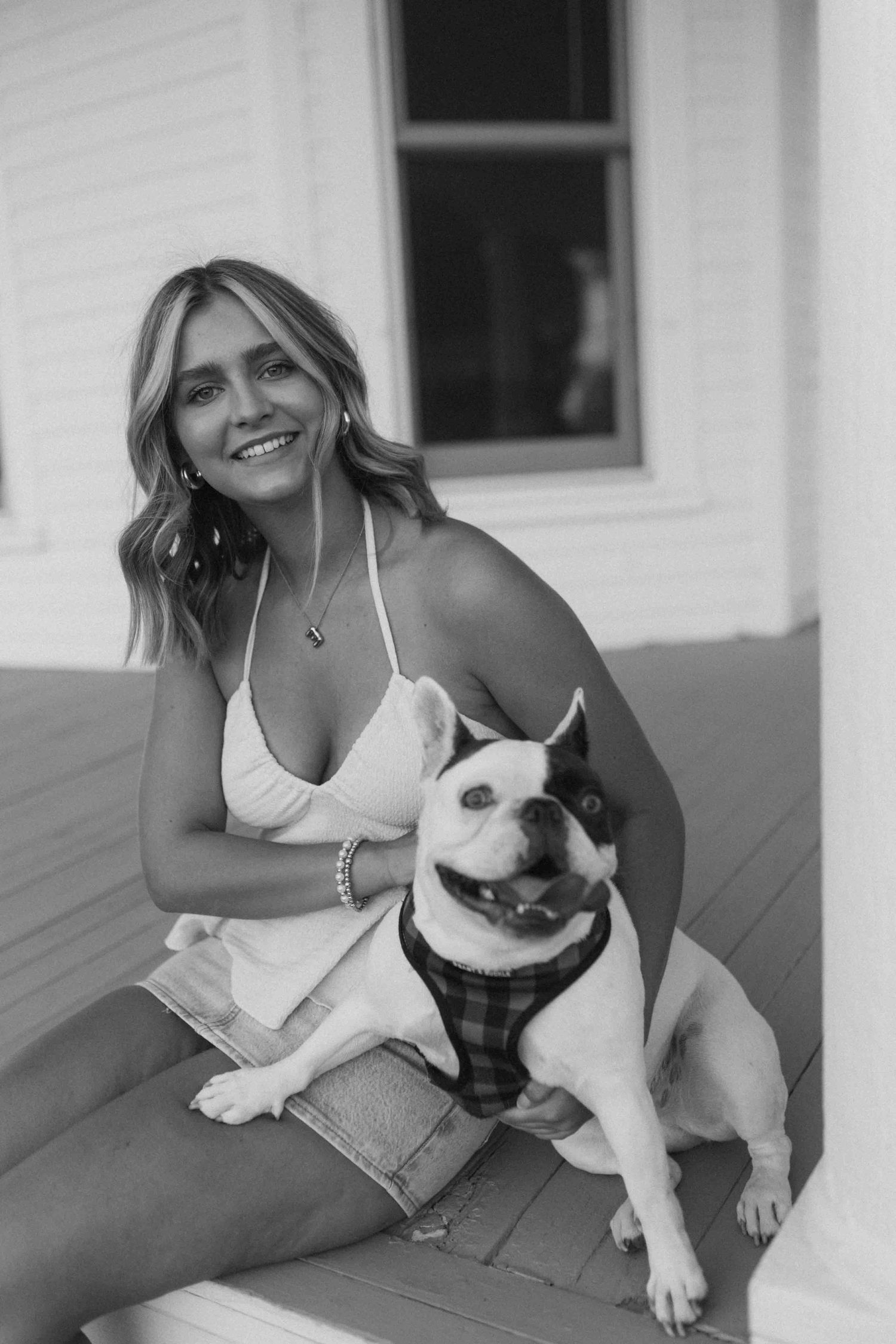 Person playing with white dog on porch in casual summer attire.