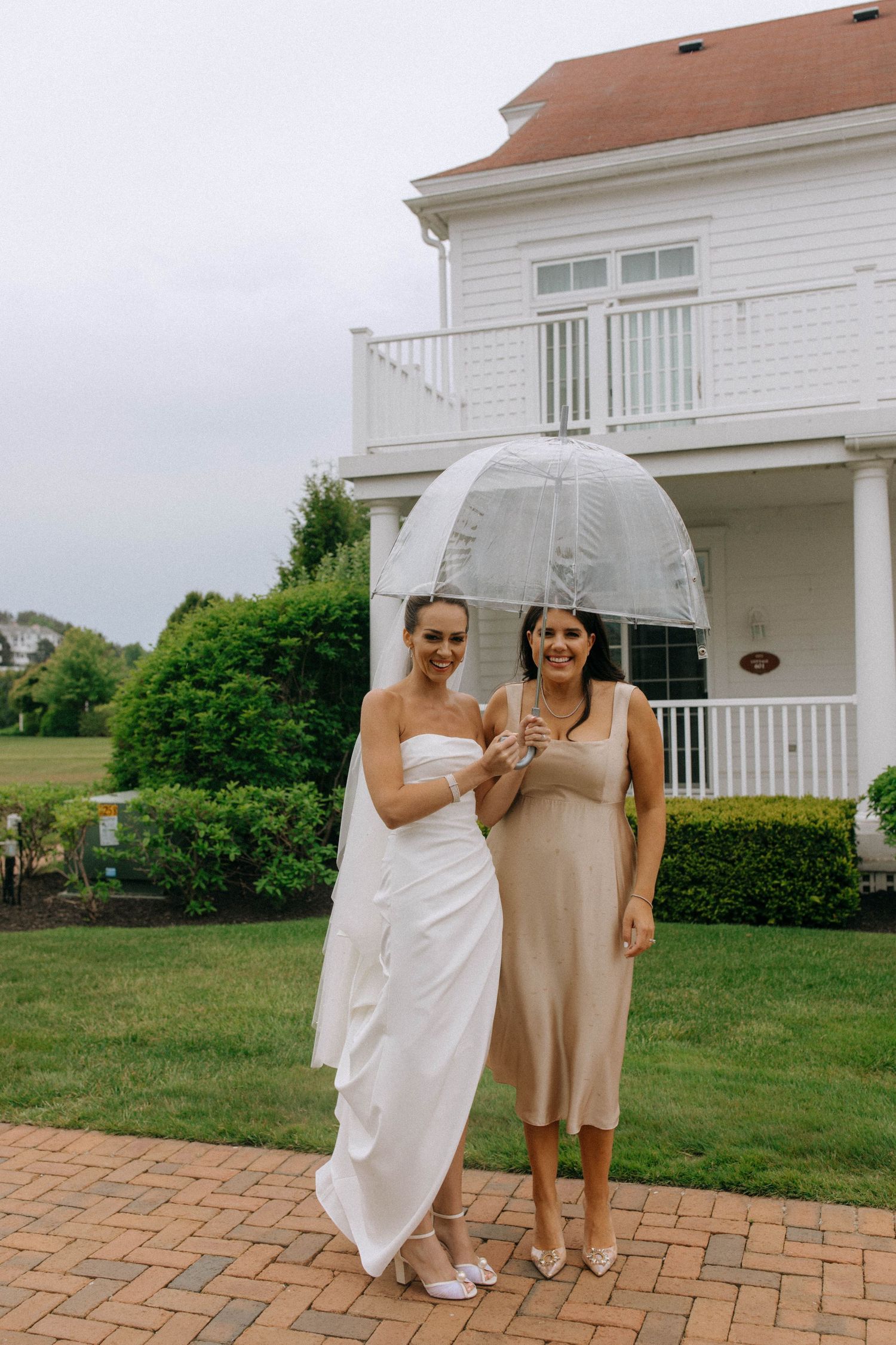 Two people share laughter under a clear umbrella outside a white coastal home.
