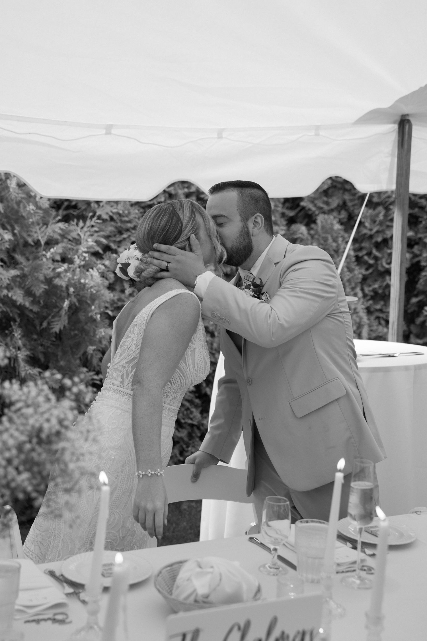 Wedding reception scene with couple sharing a kiss at an outdoor table setting.