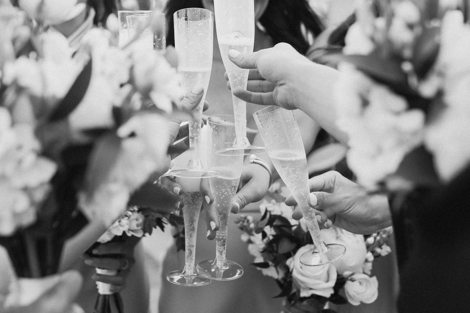 Black and white image of champagne glasses clinking during a wedding toast.