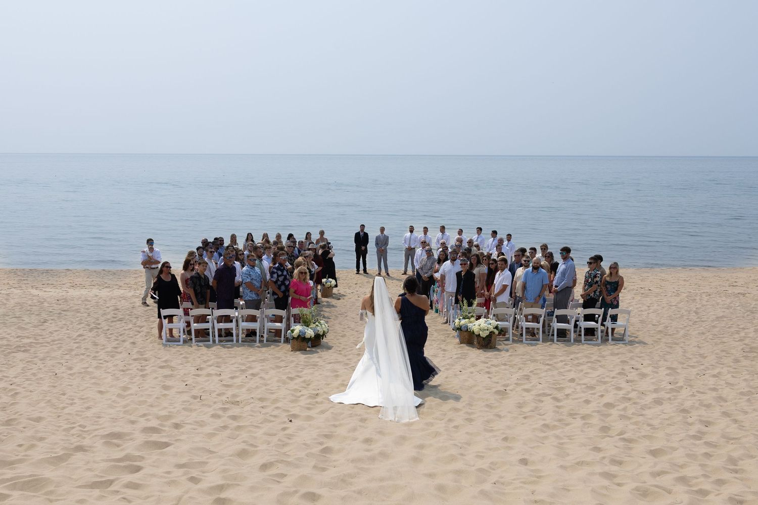 Beach wedding ceremony setup with white chairs arranged on sand facing the ocean.