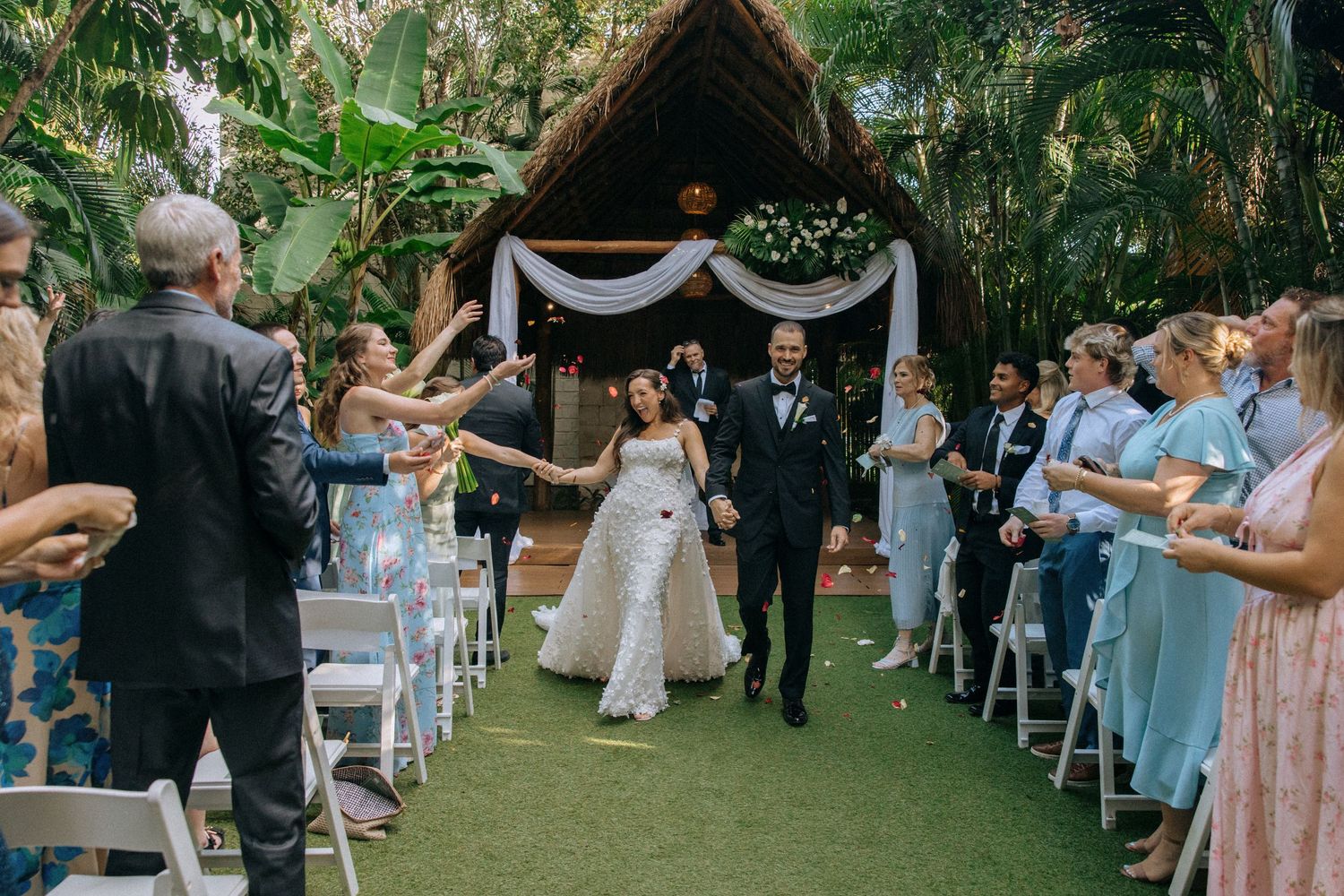 Wedding celebration in a lush garden setting with guests cheering along the aisle.