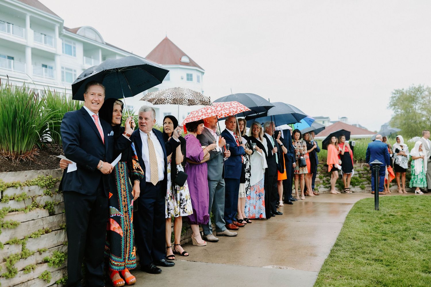 Wedding guests with umbrellas line up along a path during a rainy celebration.