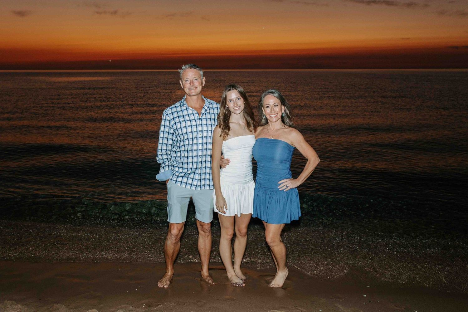 Group posing together on beach with orange sunset sky in background.