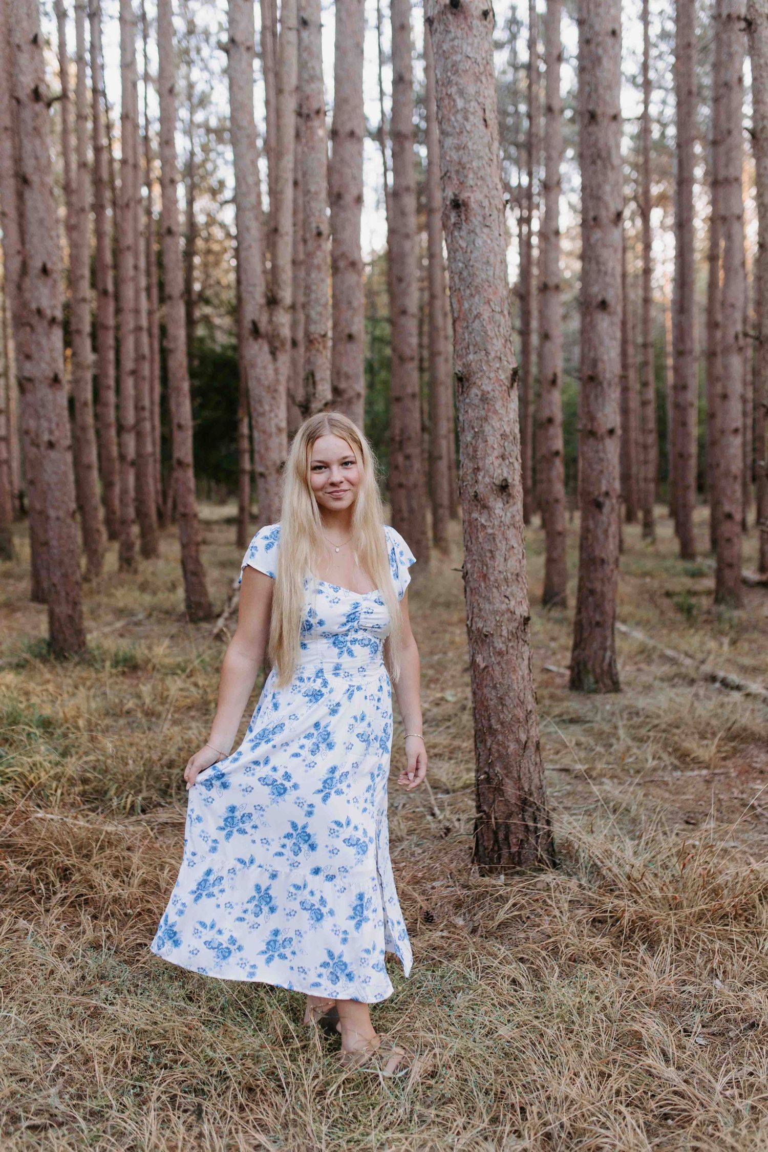 Feminine fashion portrait featuring a blue floral dress among pine trees.
