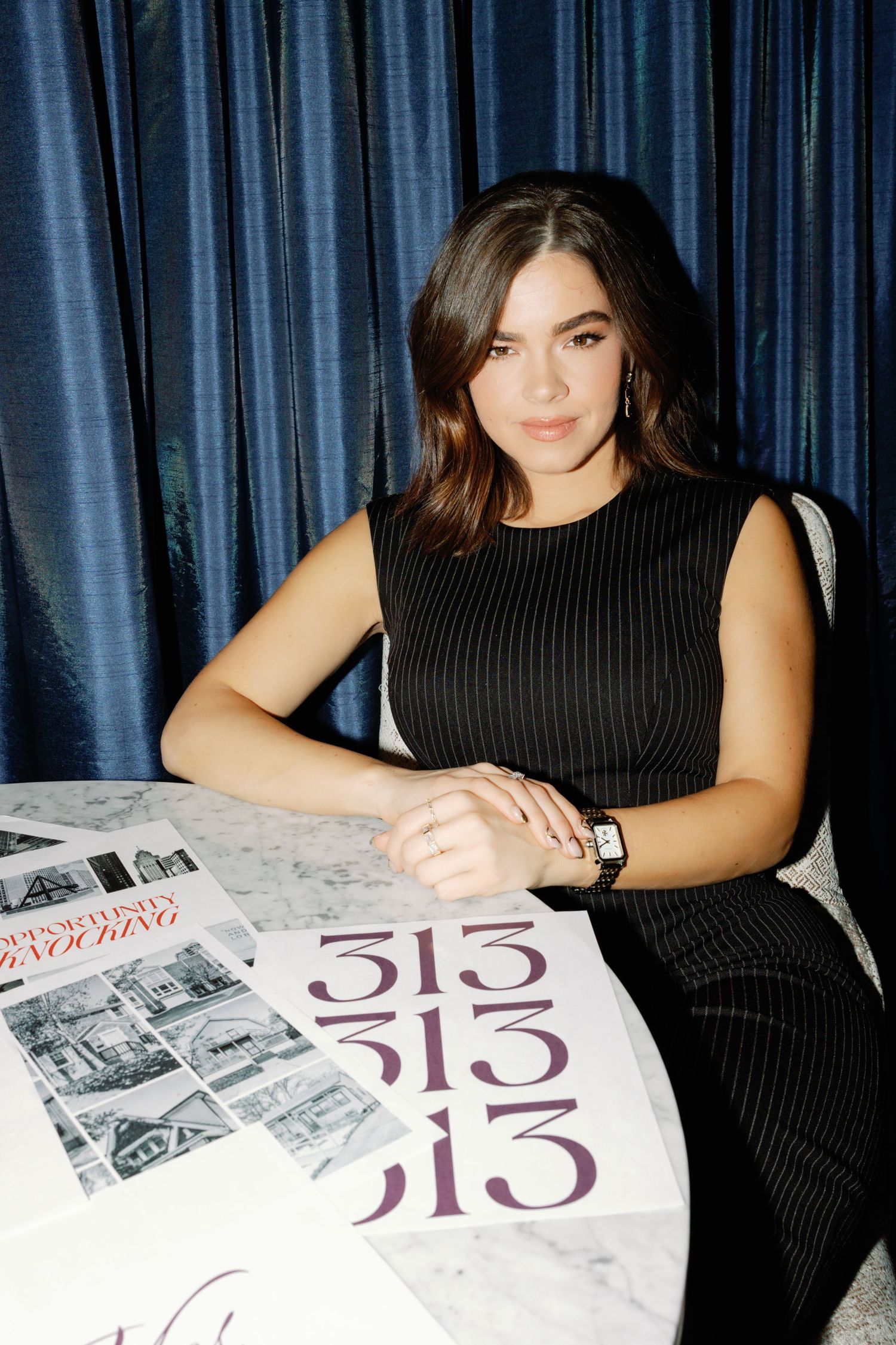 Person in black dress reviewing magazine layouts at a table.