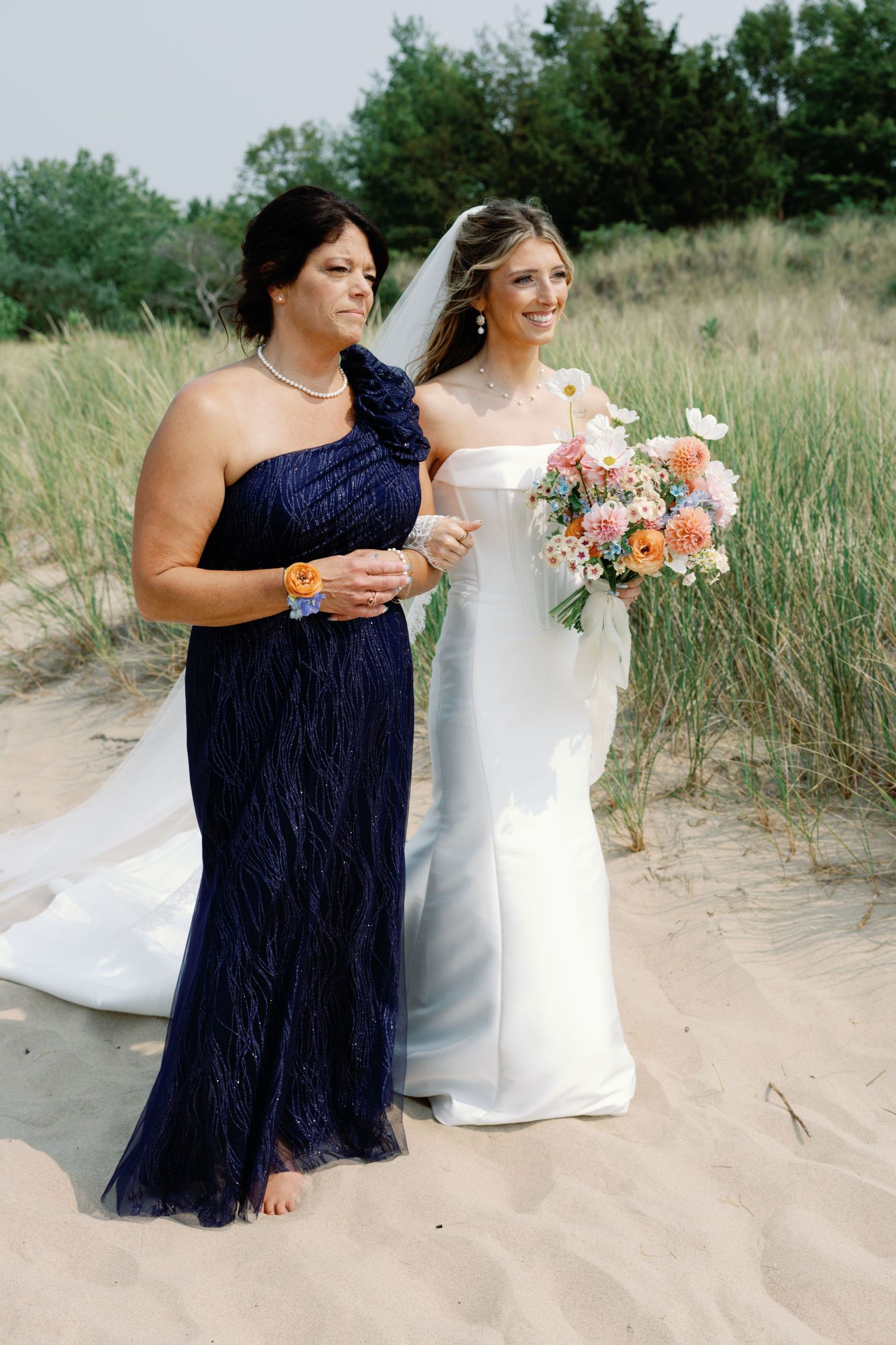 Wedding party members enjoying drinks on a beach with coastal grass.