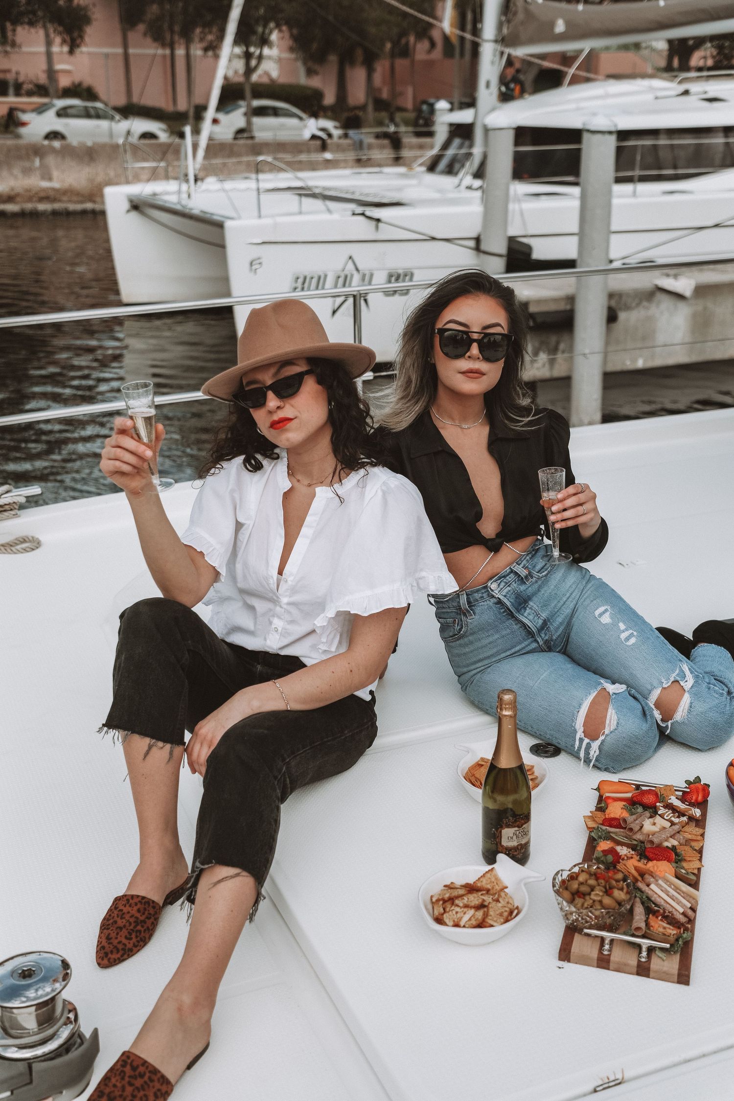 A group relaxes on a boat deck with champagne and snacks while enjoying a sunny afternoon on the water.