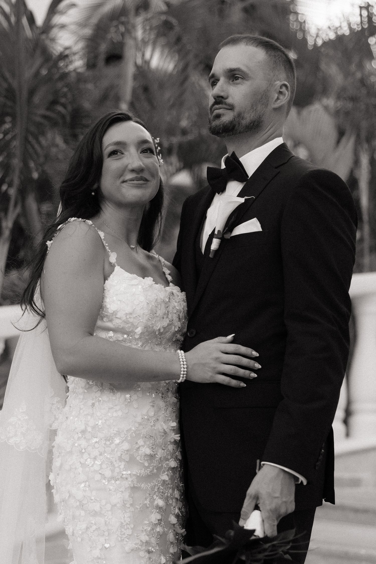 A romantic black and white wedding photo series showing a couple embracing outdoors with palm trees in the background.
