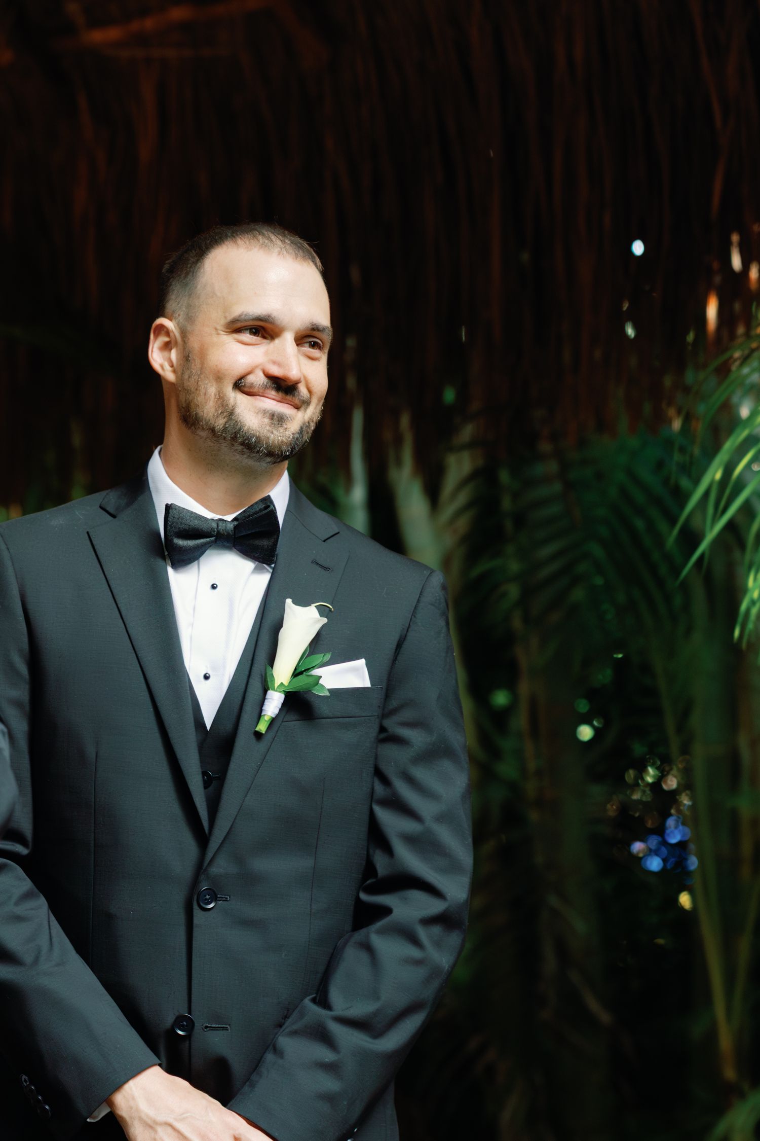 Groom in classic black tuxedo with white boutonniere smiles during wedding portraits.