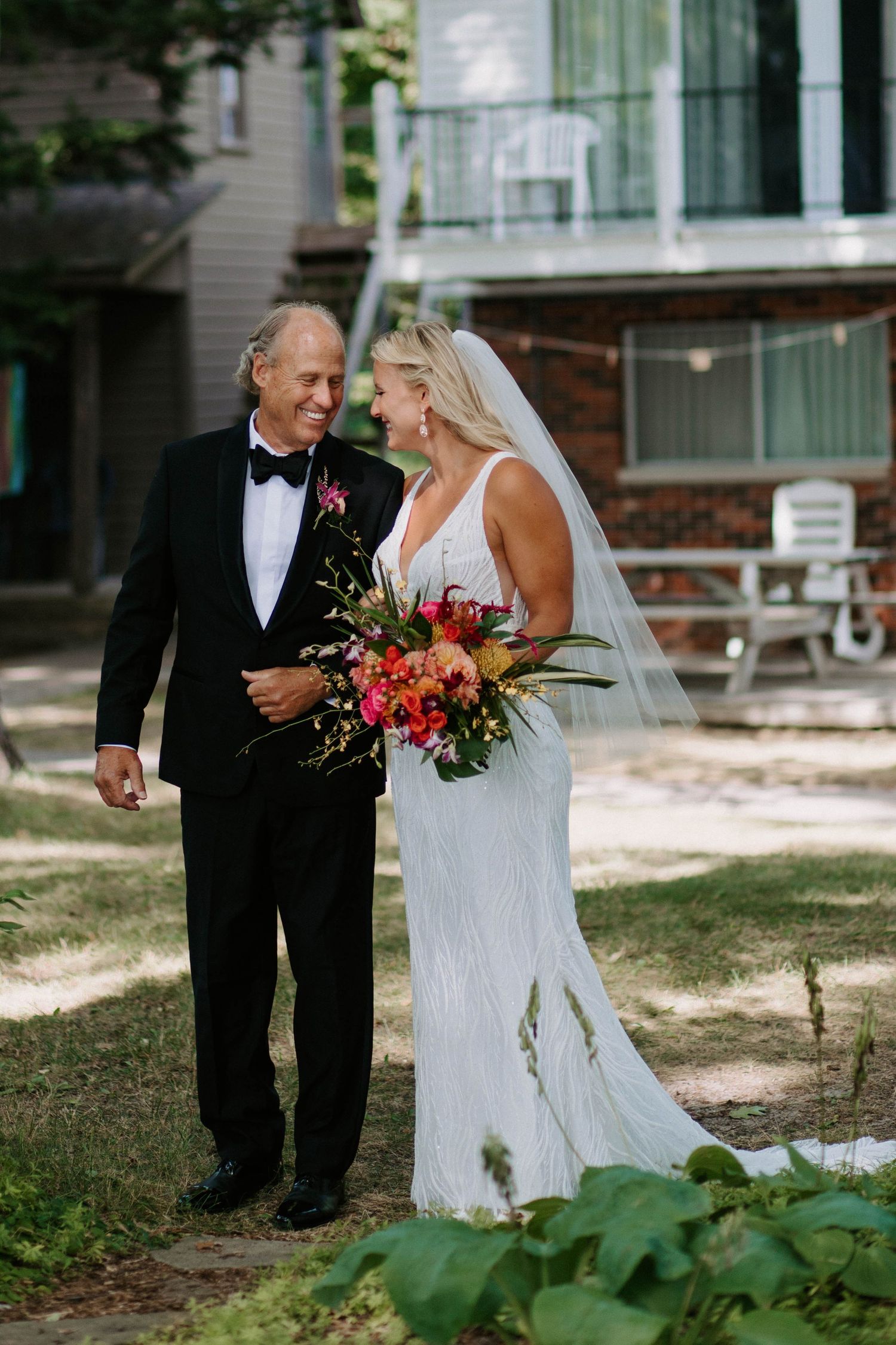 Bride in white gown and groom in tuxedo share first look moments outdoors.