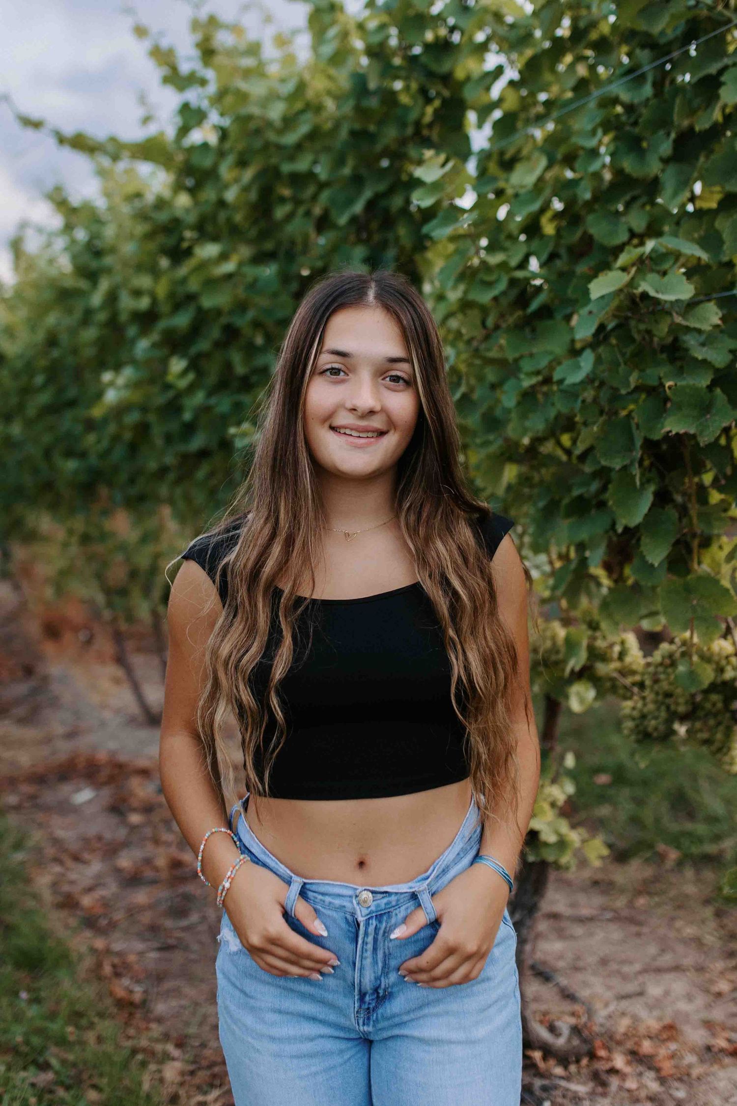 Casual outdoor photoshoot among vineyard leaves wearing denim and black top.