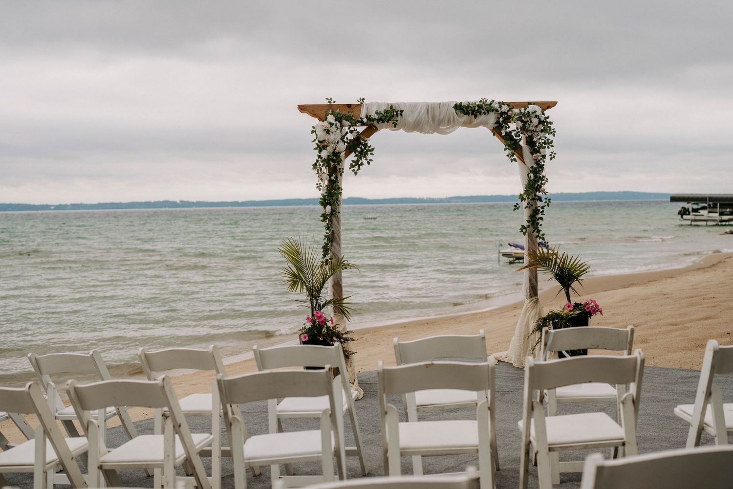 Beachfront wedding ceremony setup with white chairs and floral arch overlooking the ocean.