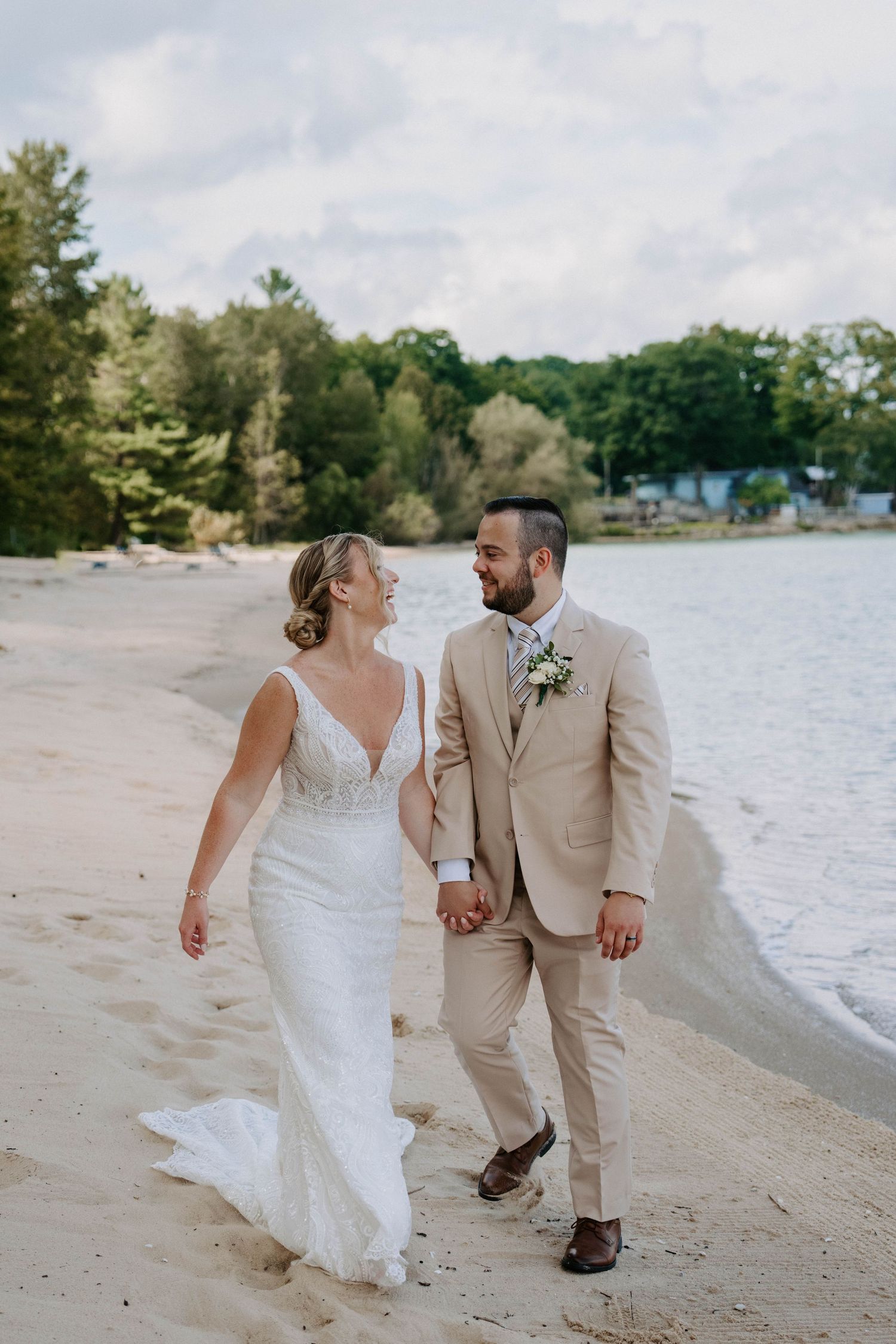 Wedding couple strolls hand in hand along a peaceful lakeside beach.