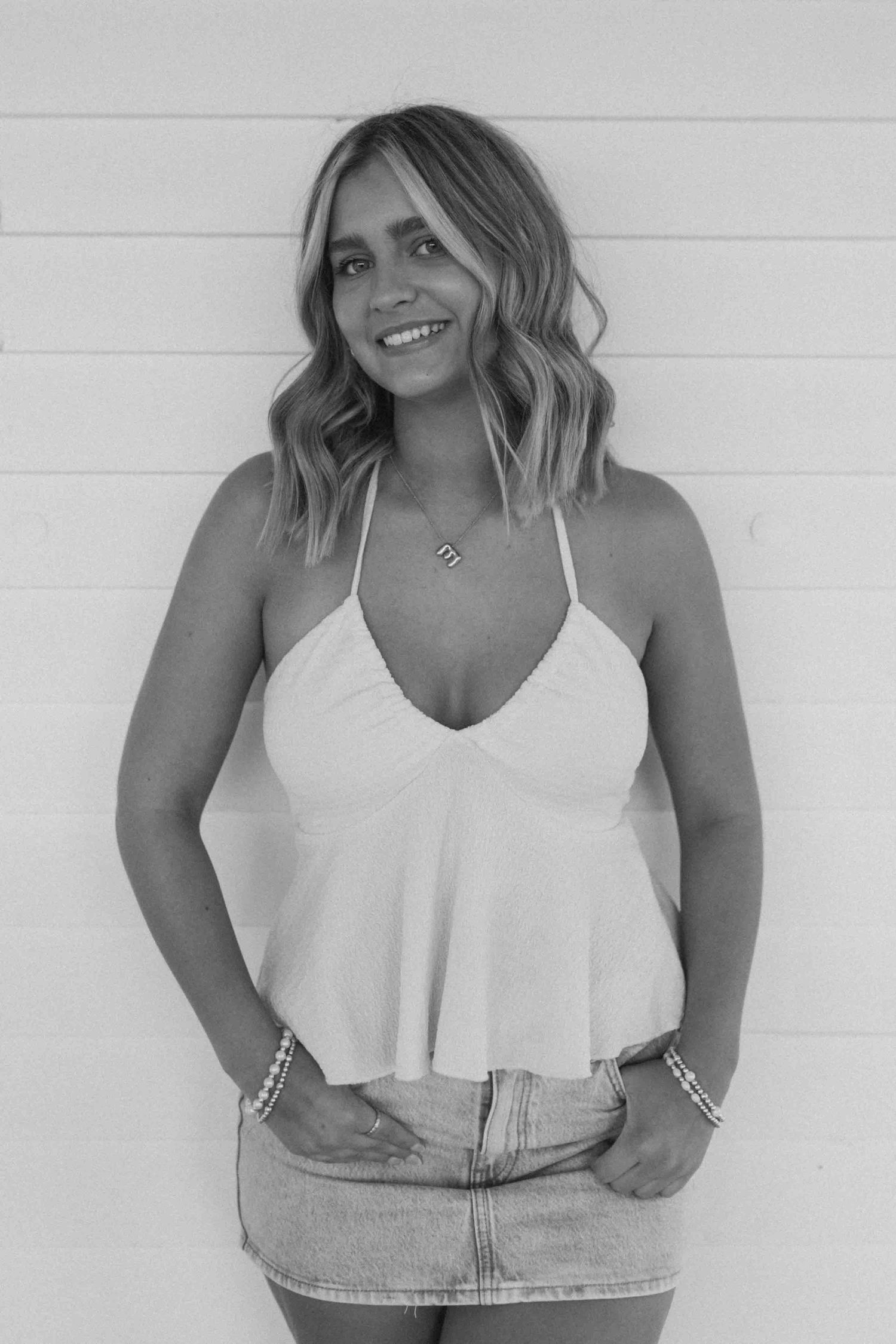 Woman in white tank top poses against white wall showing casual summer style.