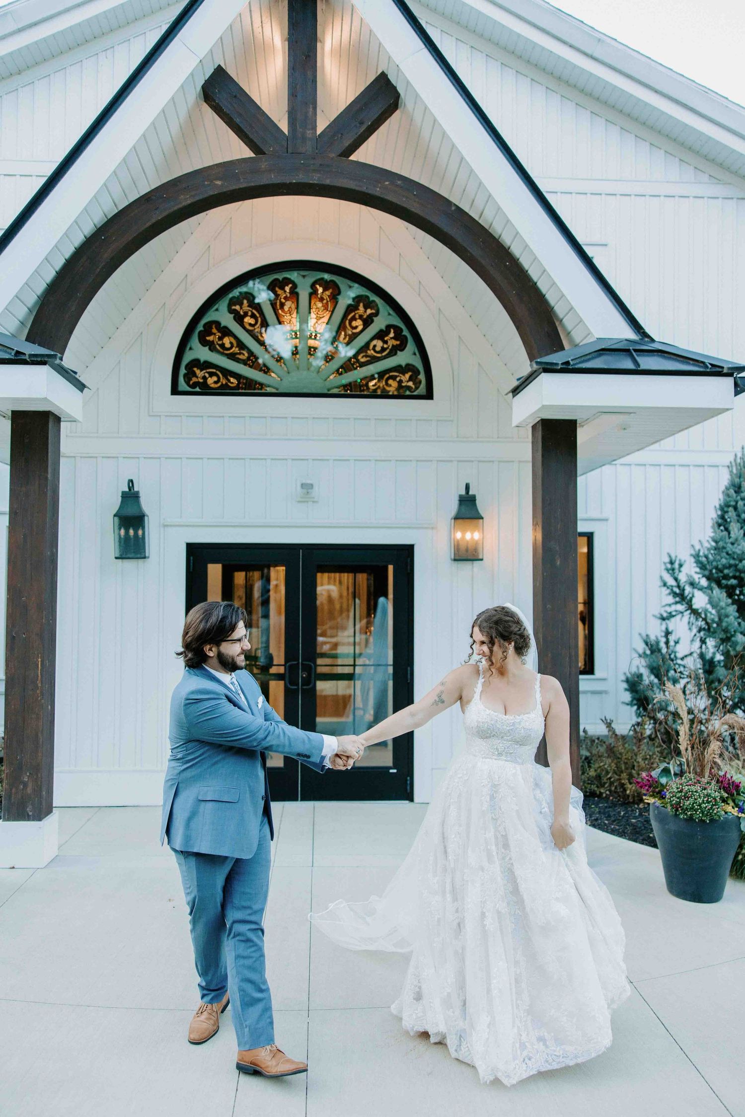 Dancing couple twirls outside a white chapel with stained glass windows.