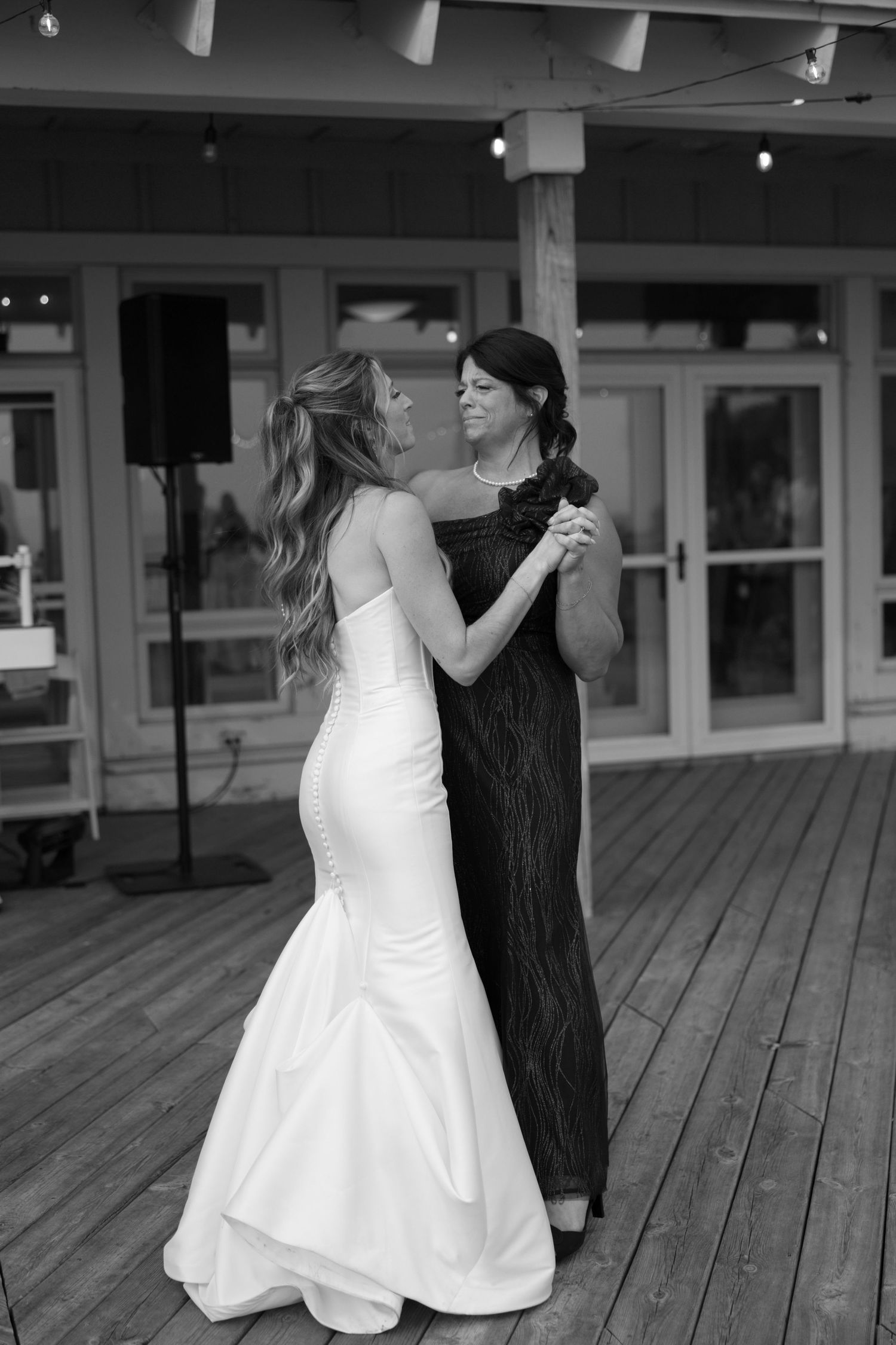 A couple shares their first dance on a wooden deck at their wedding reception.