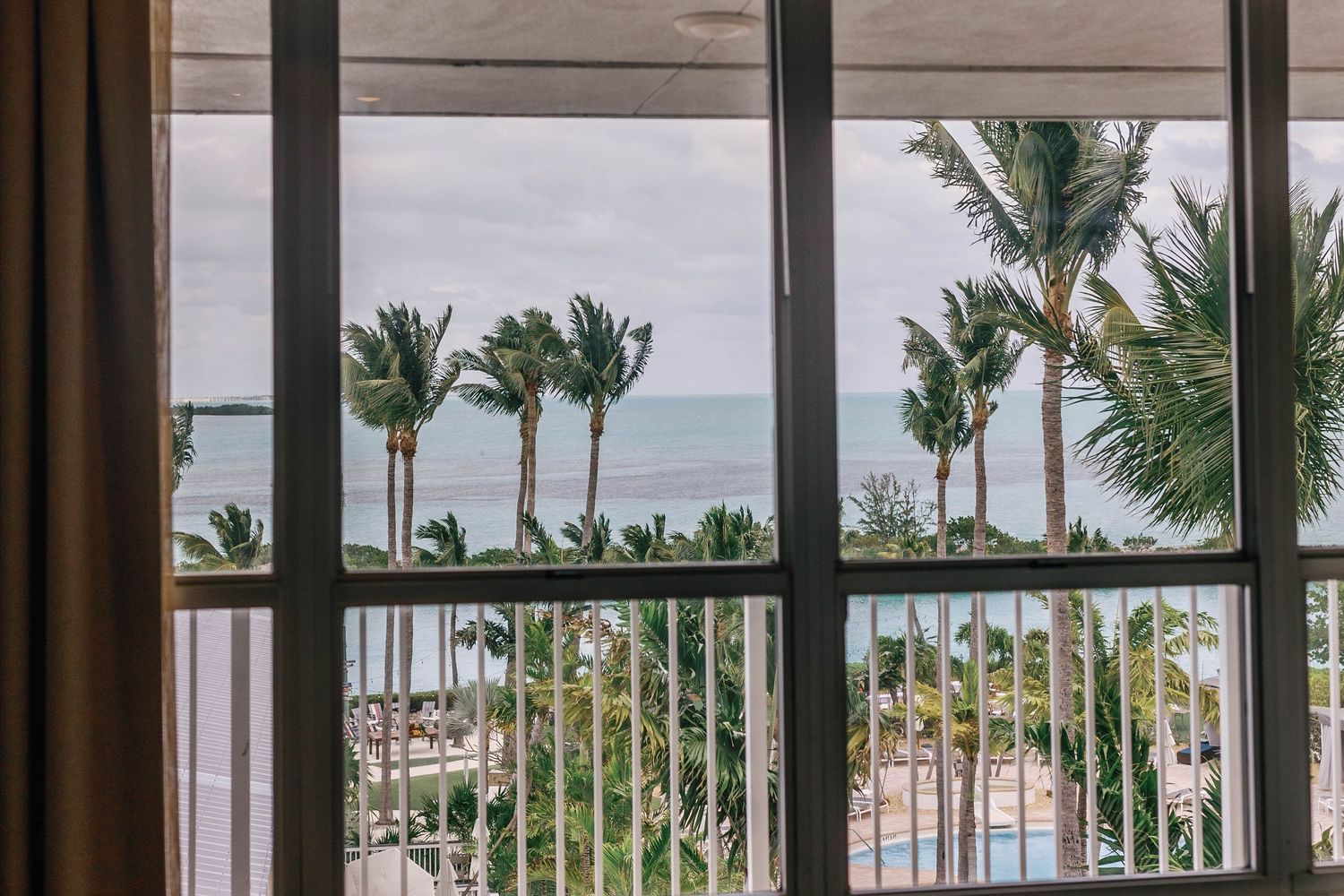 Luxury hotel lobby with floor-to-ceiling windows overlooking palm trees and ocean views.
