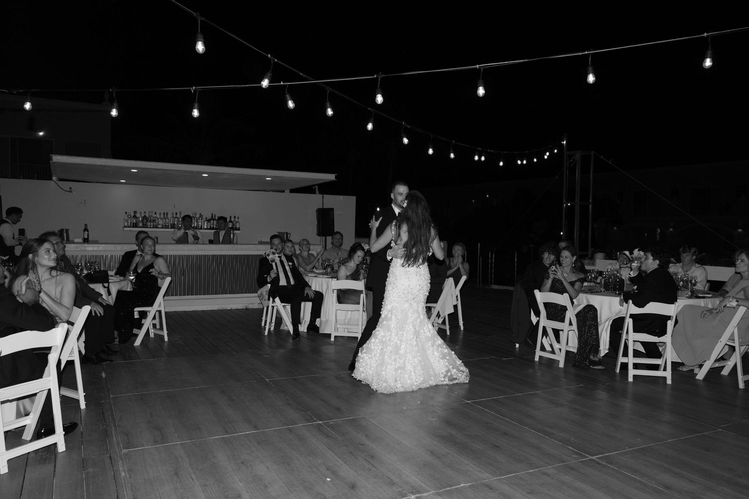 Black and white photo of bride dancing at reception with guests seated at white tables.