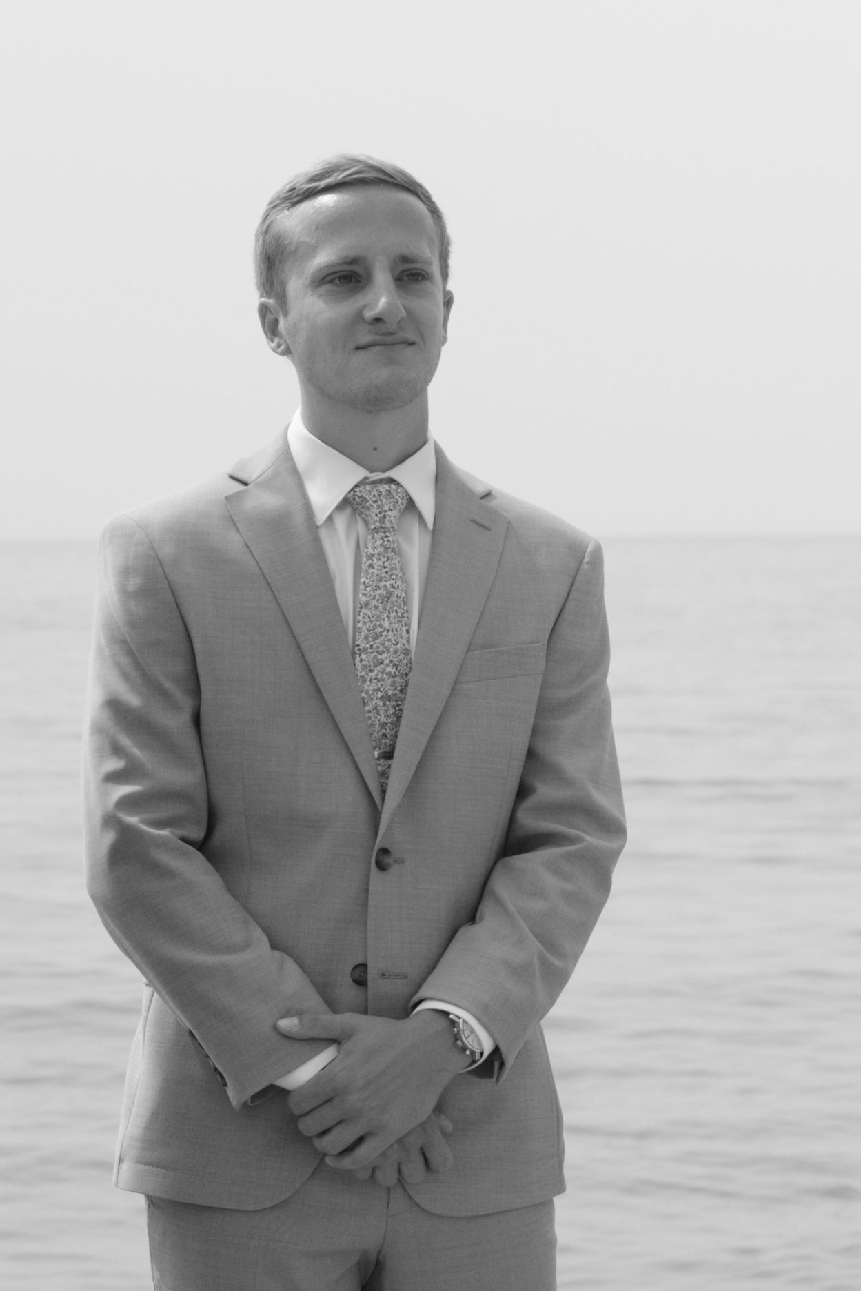 Groom in gray suit and floral tie poses for portraits near the ocean.