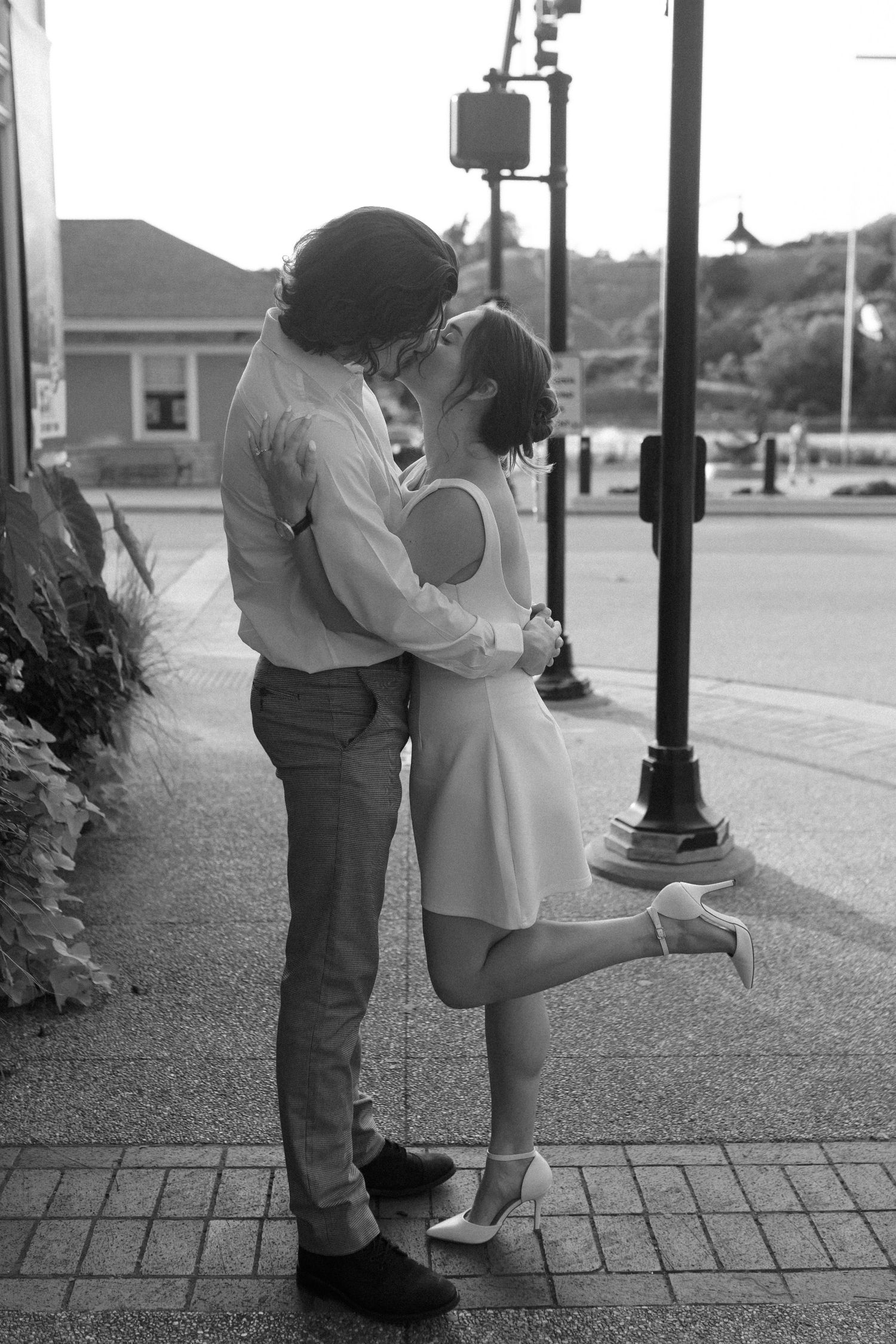Black and white photo of a couple sharing a romantic kiss on a street corner.