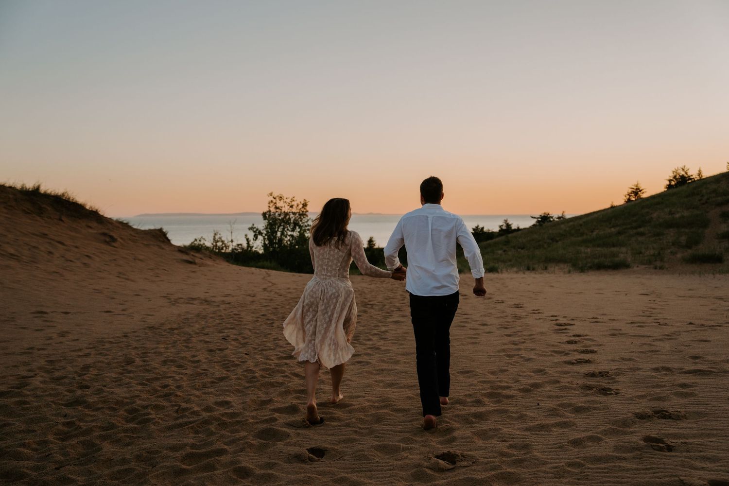 Silhouettes walk along a beach path during sunset with warm orange sky.