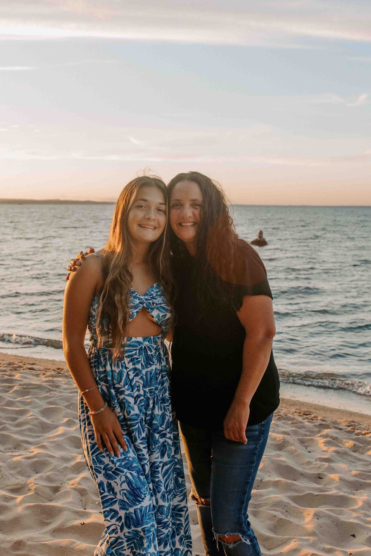 Two people share a joyful moment on a sandy beach at sunset with the ocean in the background.