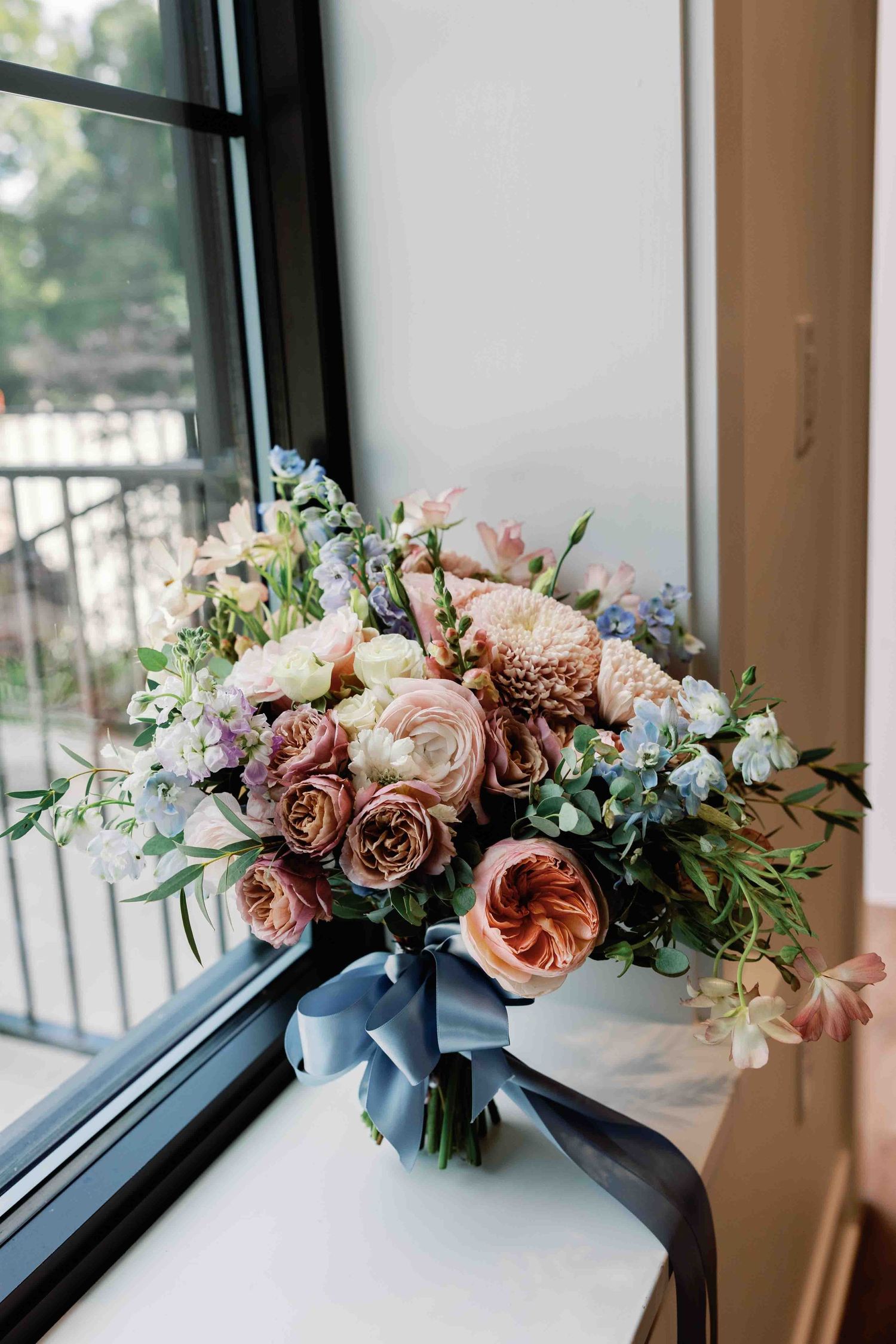 Romantic floral arrangements in dusty blue and pink tones displayed along a windowsill.