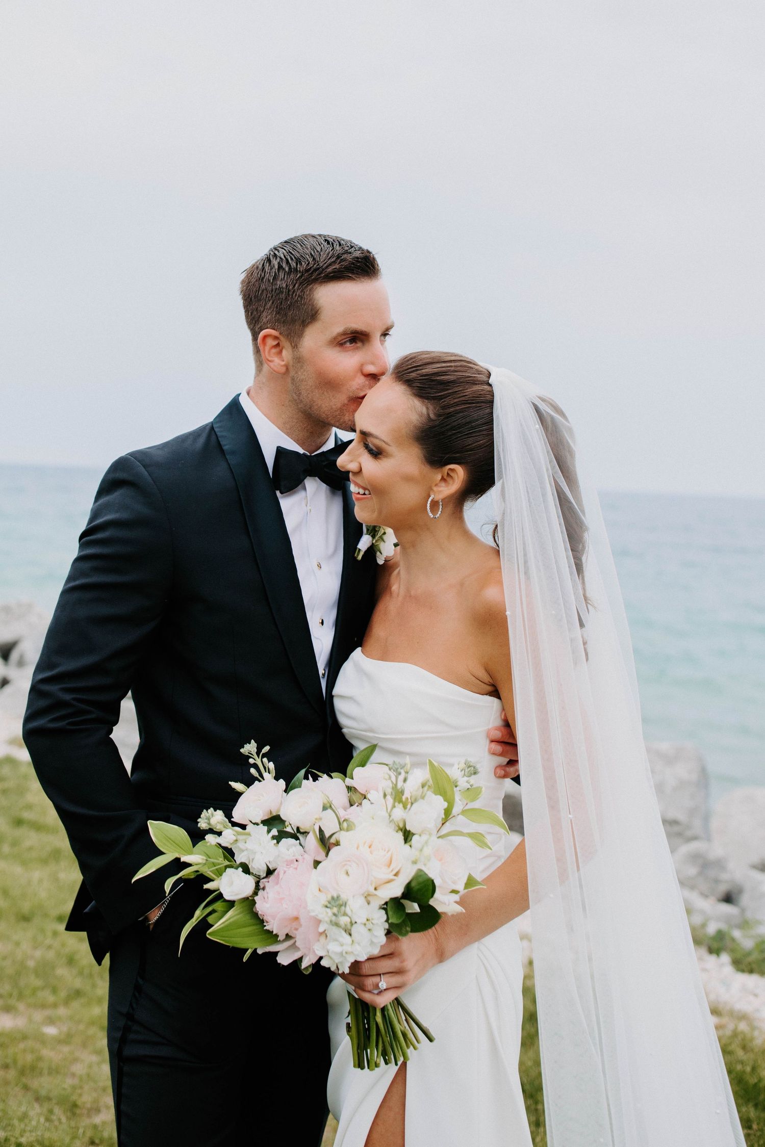 Intimate wedding portraits captured against a serene ocean backdrop with white floral bouquet.
