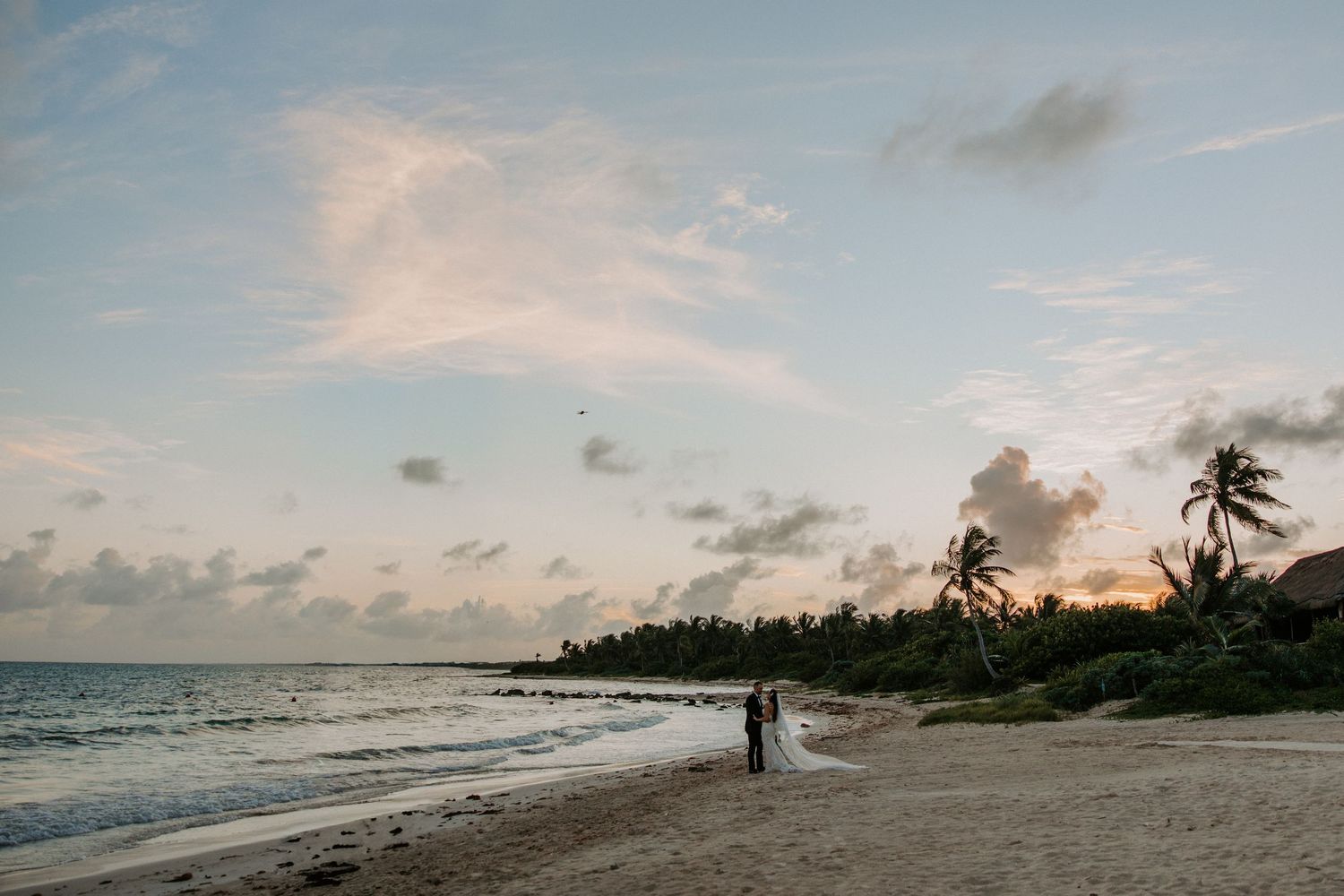 Wide angle beach landscape with palm trees and clouds during a sunset wedding ceremony.