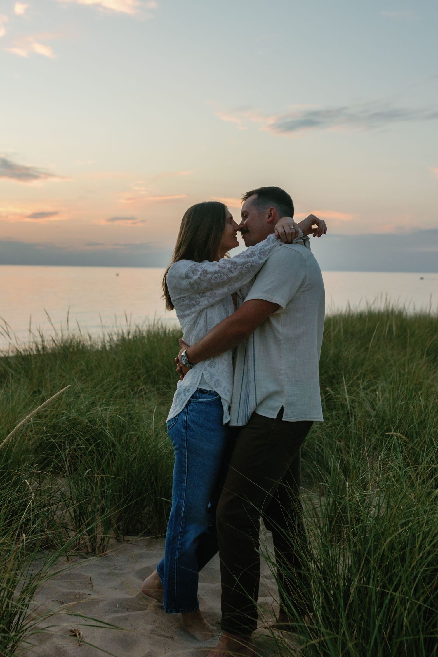 Romantic couple embracing in tall grass at sunset on a beach.
