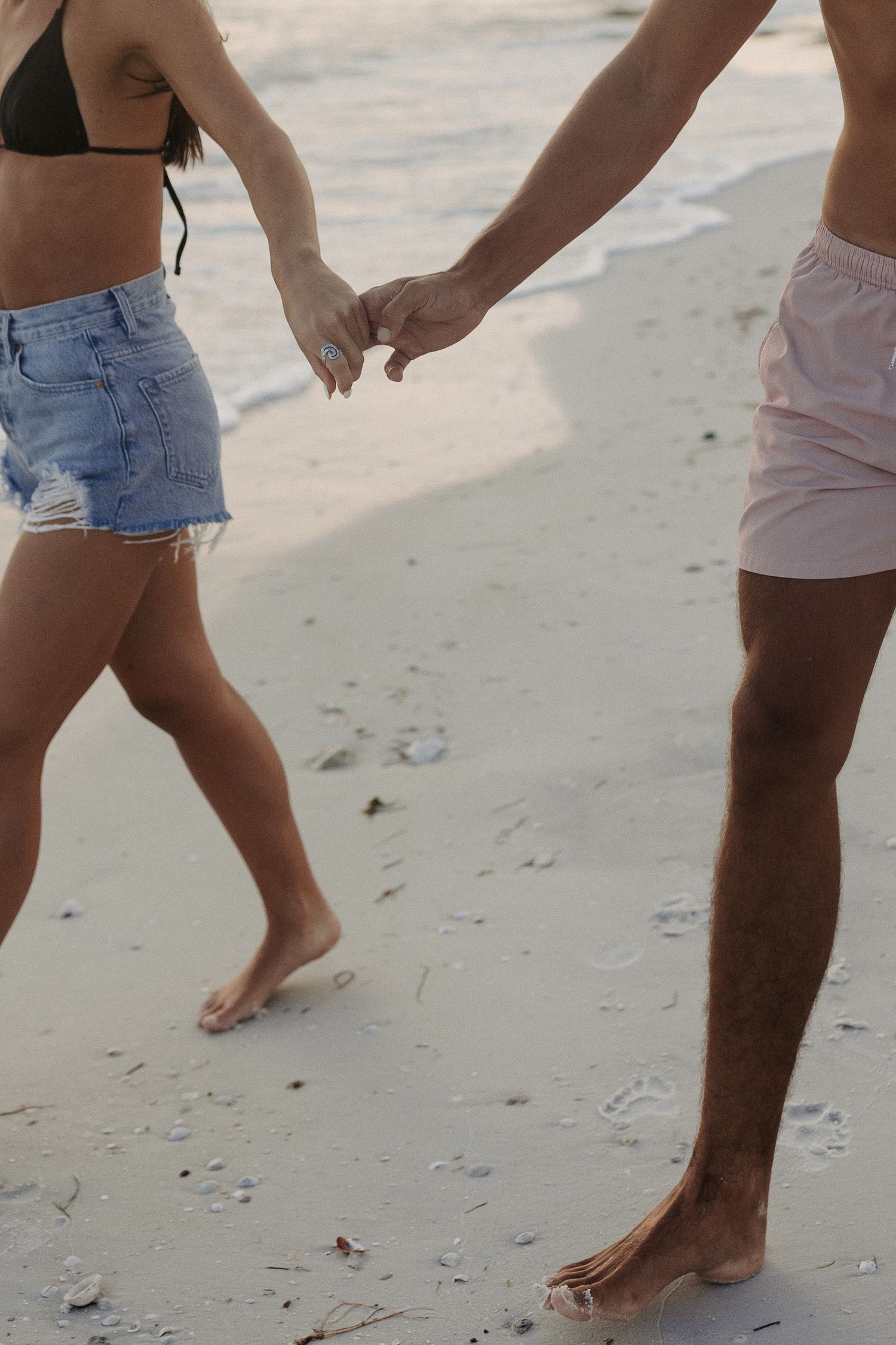 Bare feet of people walking together on a sandy beach during sunset.