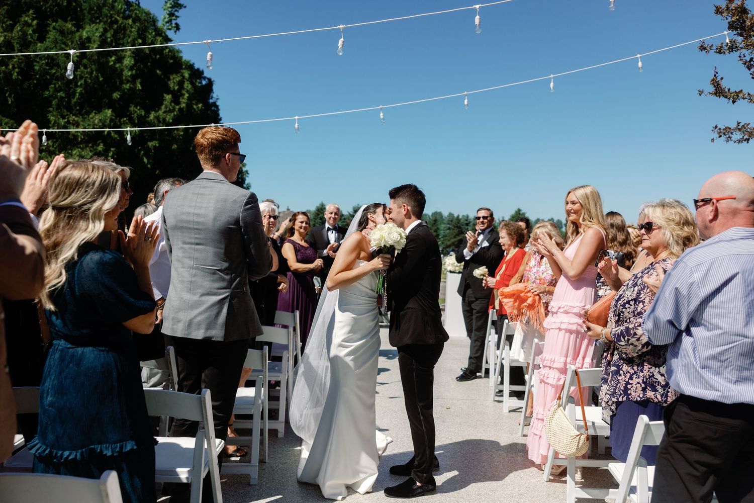 Outdoor wedding ceremony guests gathered under string lights.
