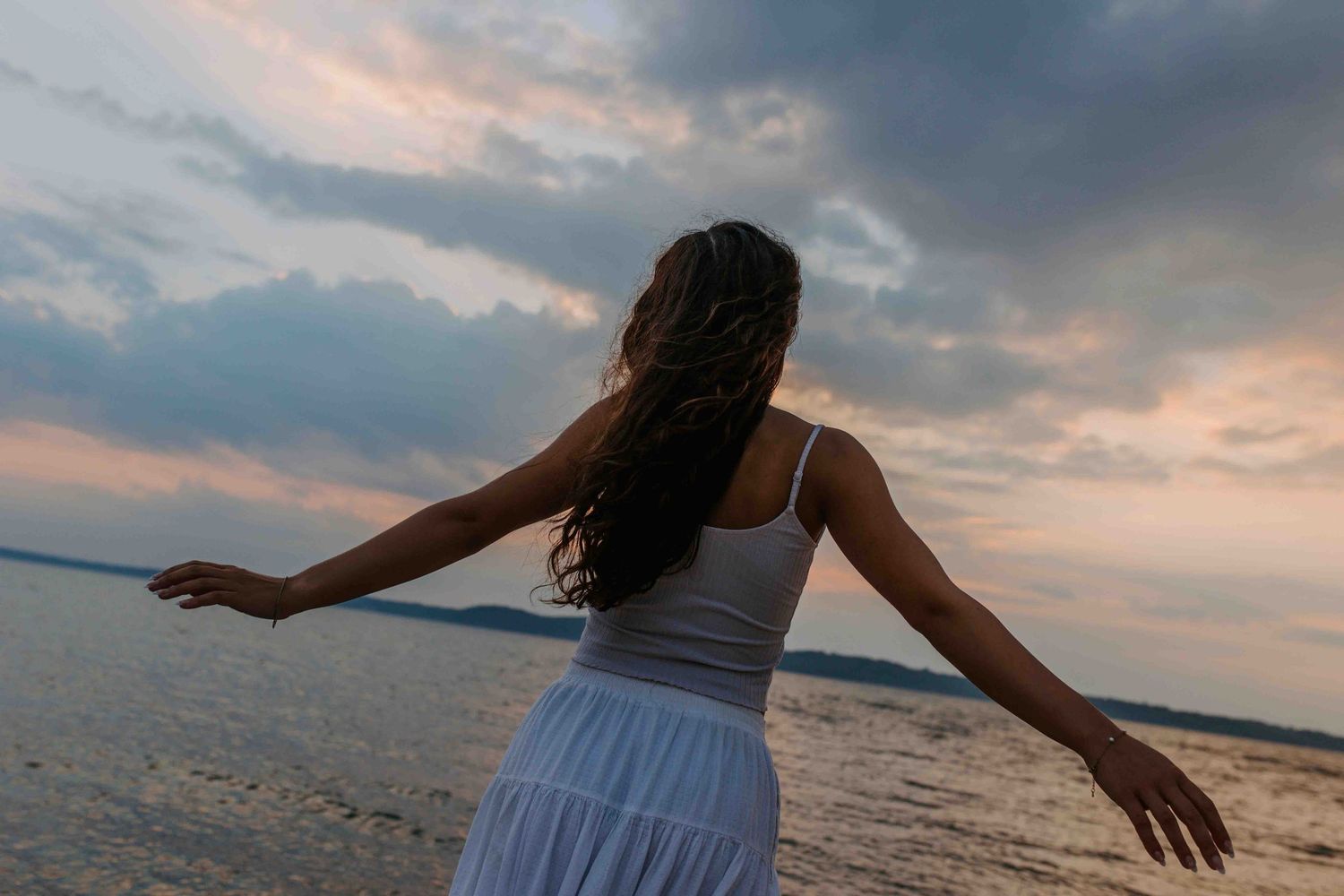 Silhouette of woman dancing against dramatic sunset sky at beach.