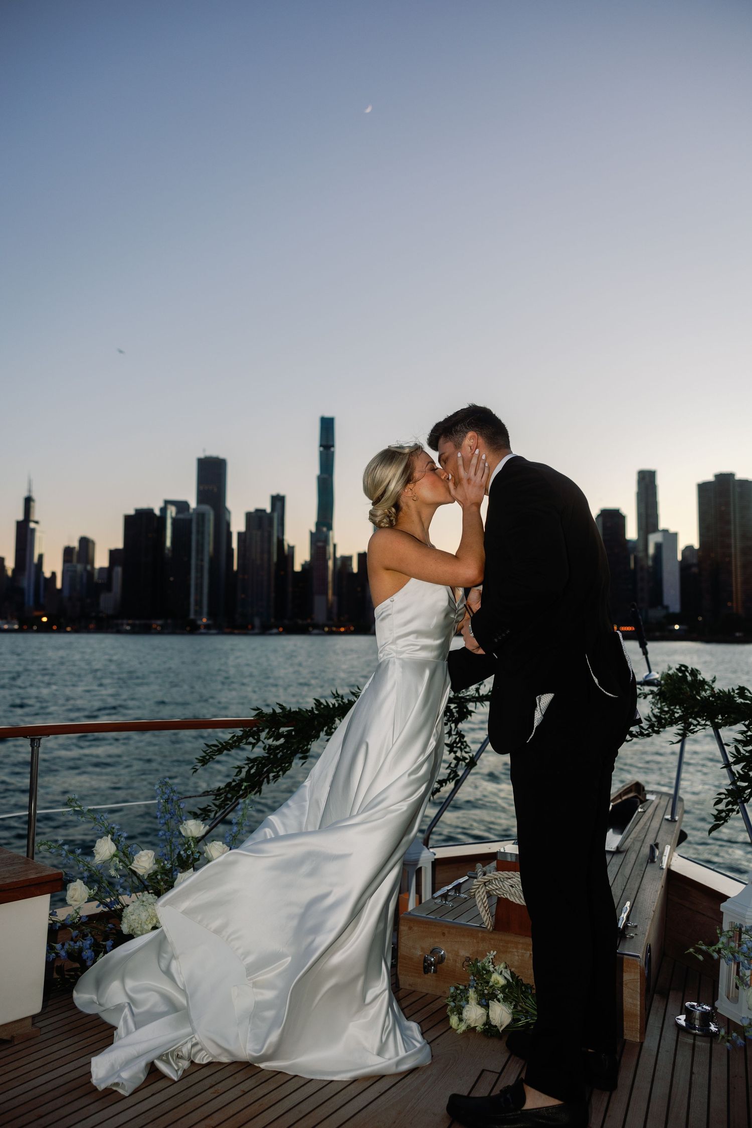 Wedding couple sharing romantic moments on boat deck with Chicago skyline at dusk.