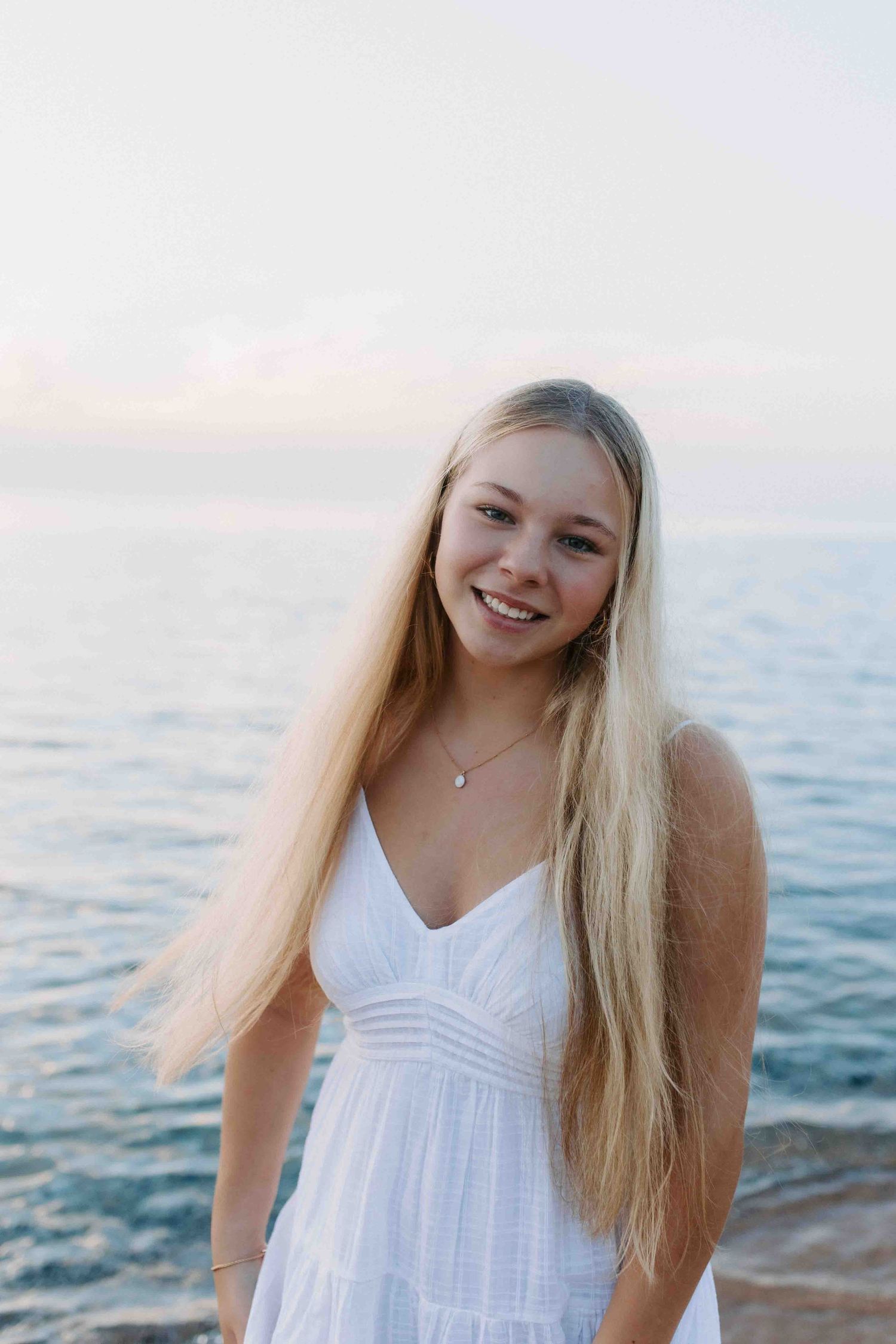 A casual beachside photoshoot featuring someone in a flowing white sundress against the ocean backdrop.