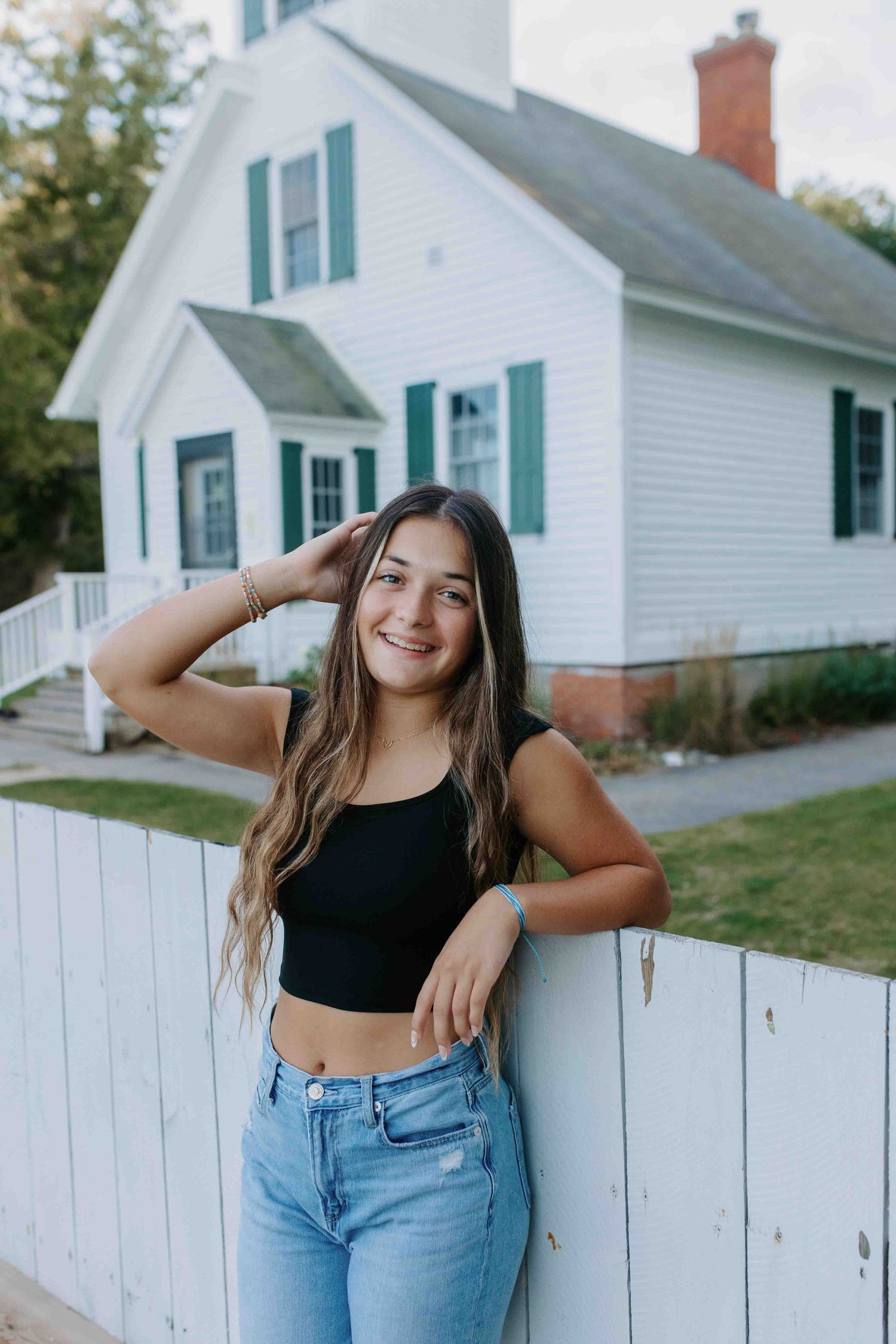 Casual poses against white picket fence with farmhouse in background.