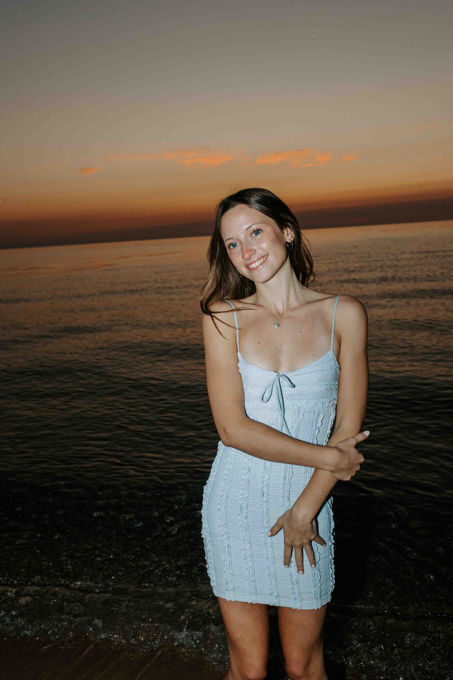 Sunset photoshoot on the beach featuring light blue summer dress against orange sky.