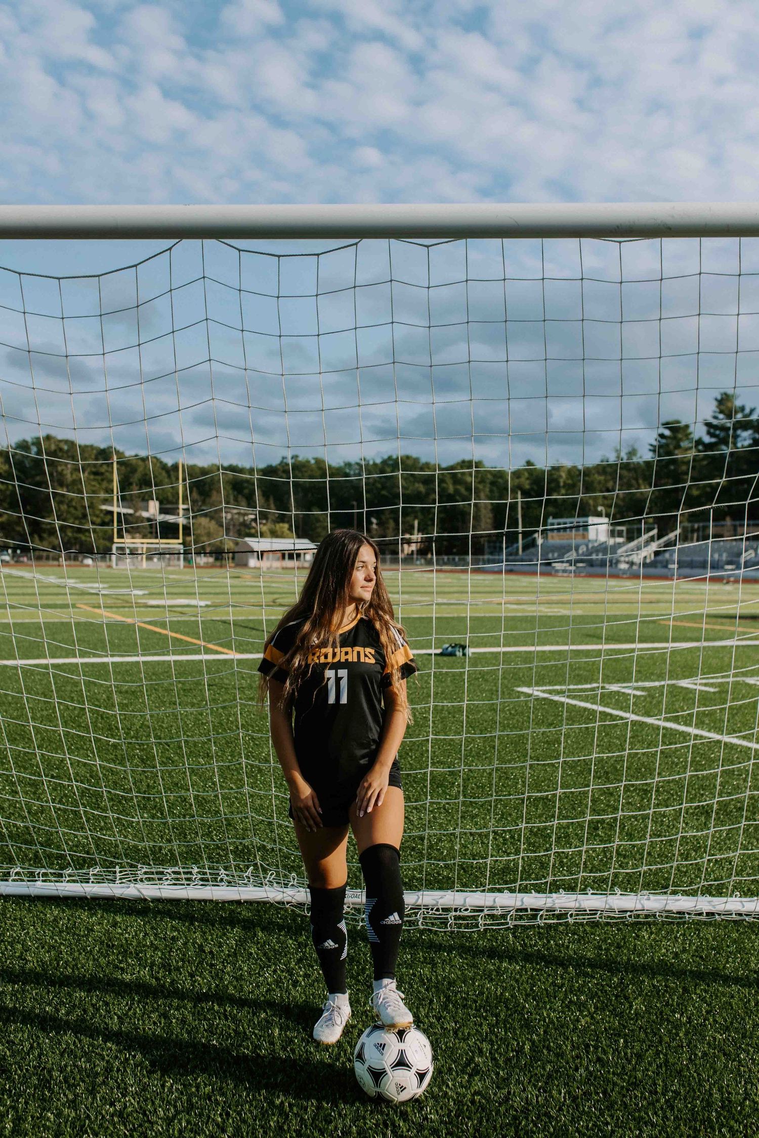 Soccer player posing with ball near goal on sunny field.