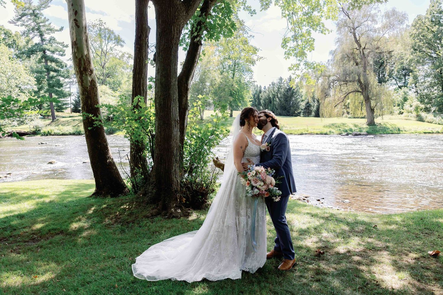 Wedding party poses for photos in a scenic outdoor location with trees and natural lighting.
