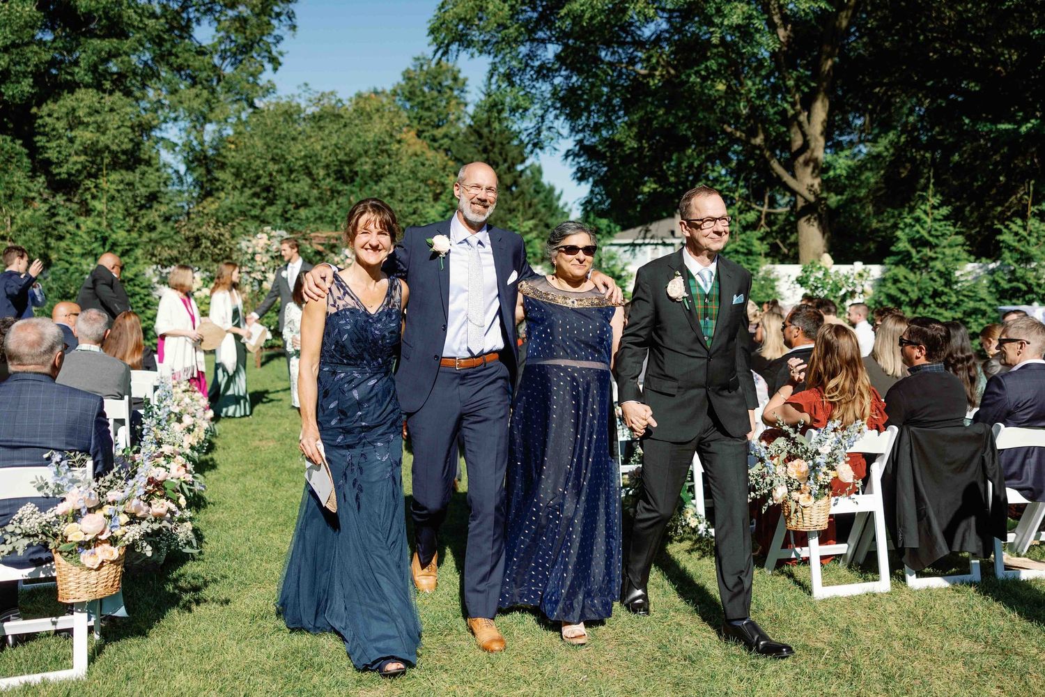 Wedding guests seated in rows of white chairs during an outdoor garden ceremony.
