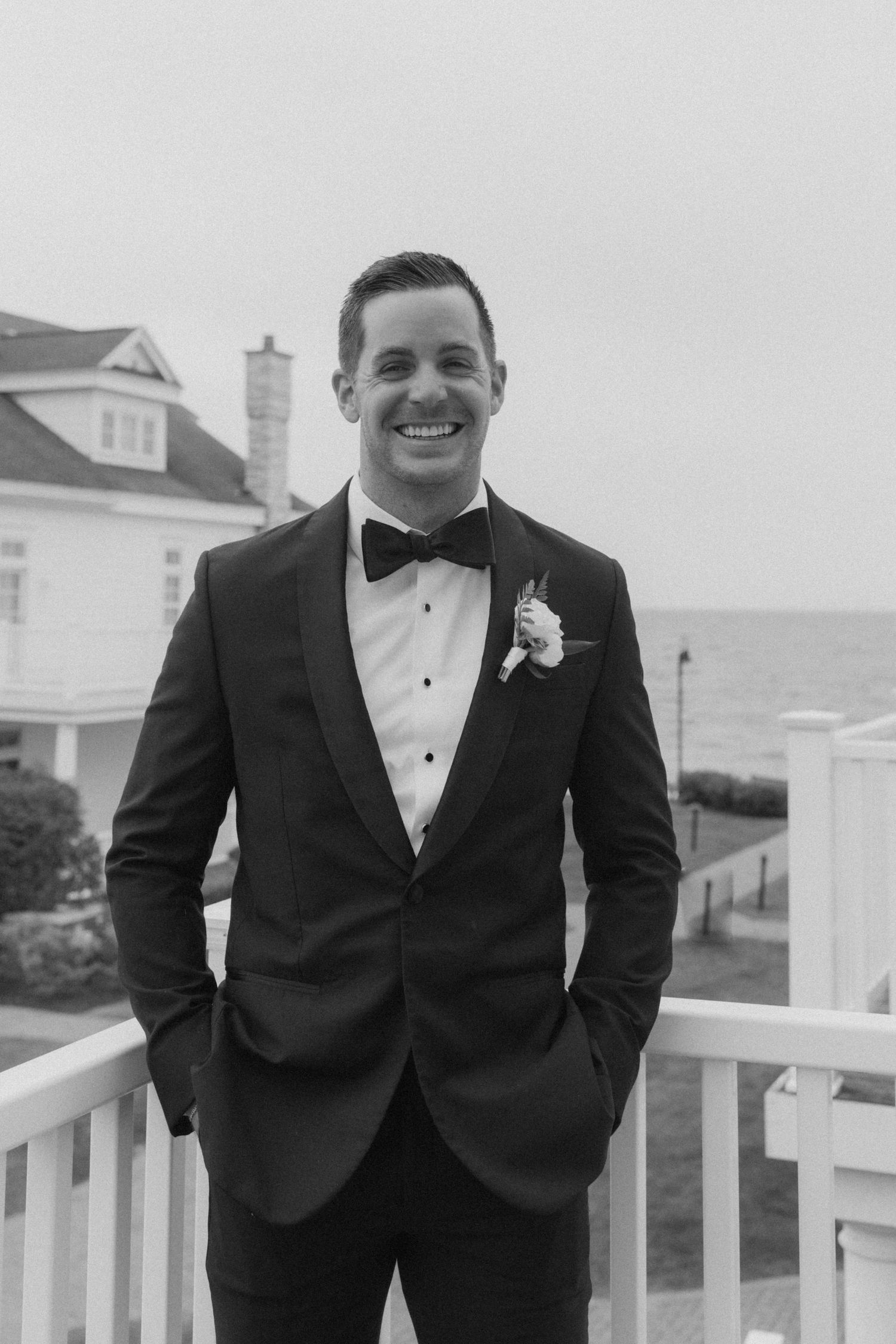 Classic black tuxedo and bowtie wedding attire on seaside deck.