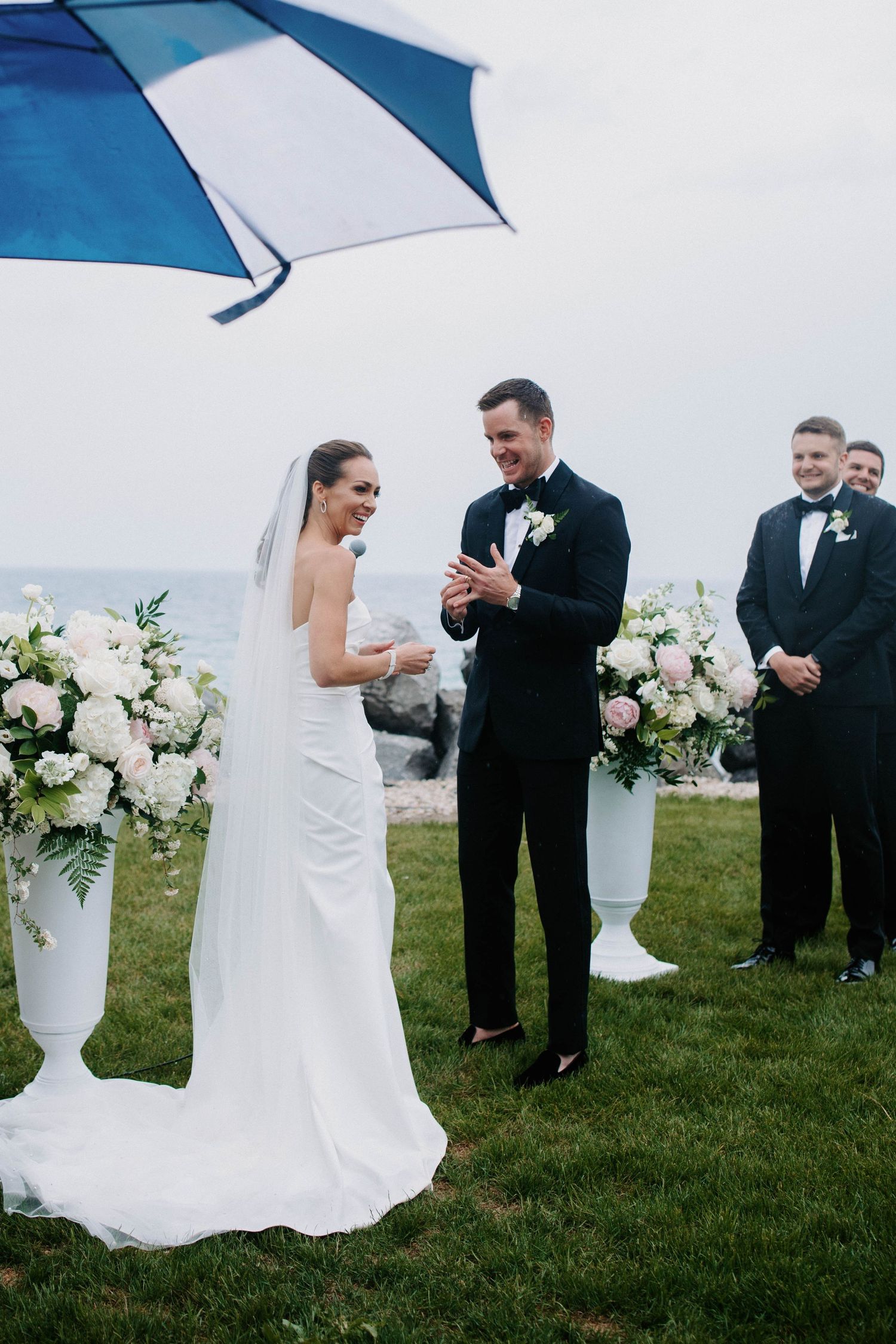 Outdoor wedding ceremony on grass with blue and white umbrellas and elegant floral decorations.
